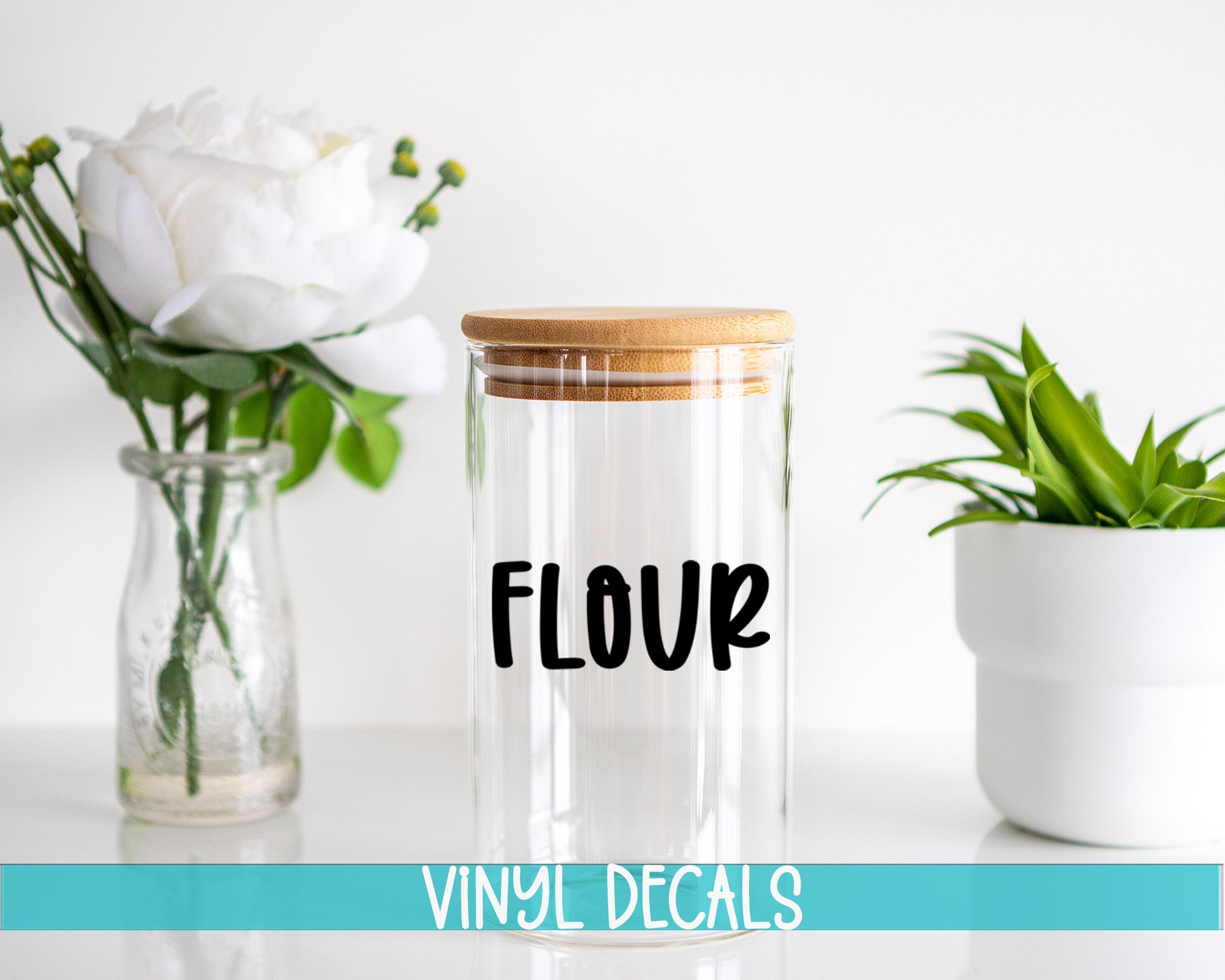 a clear glass jar with a wooden lid, a glass vase with white flowers, and a white pot with a green plant, all placed on a white surface.
