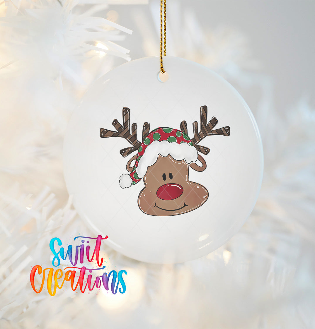A white ornament with a cartoon reindeer wearing a red and green hat, hanging on a string.