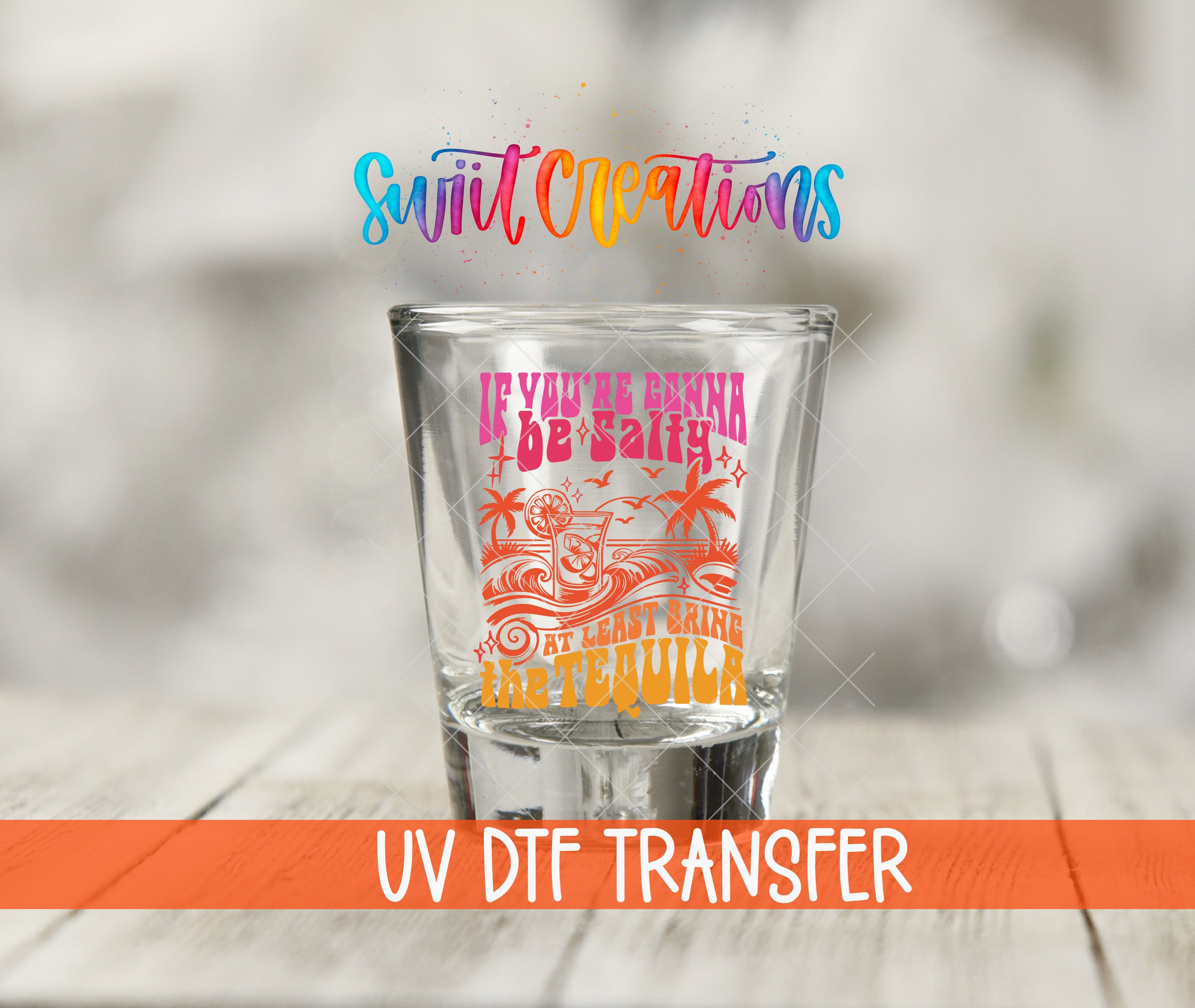 A shot glass with a colorful design and text printed on it, placed on a wooden surface.