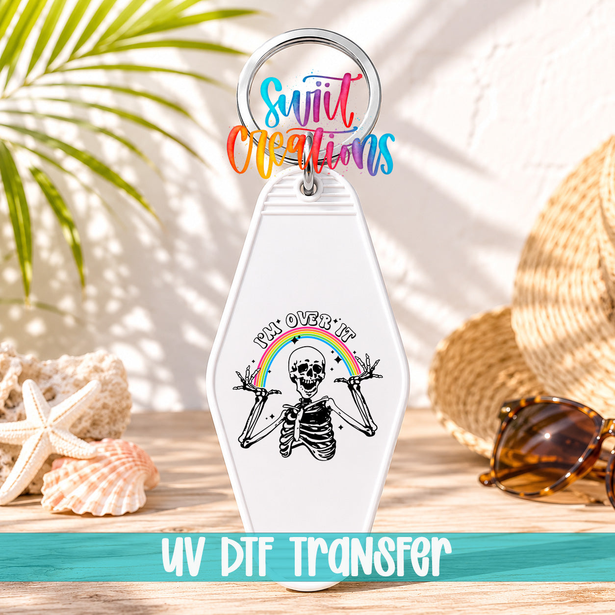 A keychain with a skeleton graphic and a rainbow graphic, along with sunglasses and a straw hat, all placed on a wooden surface.