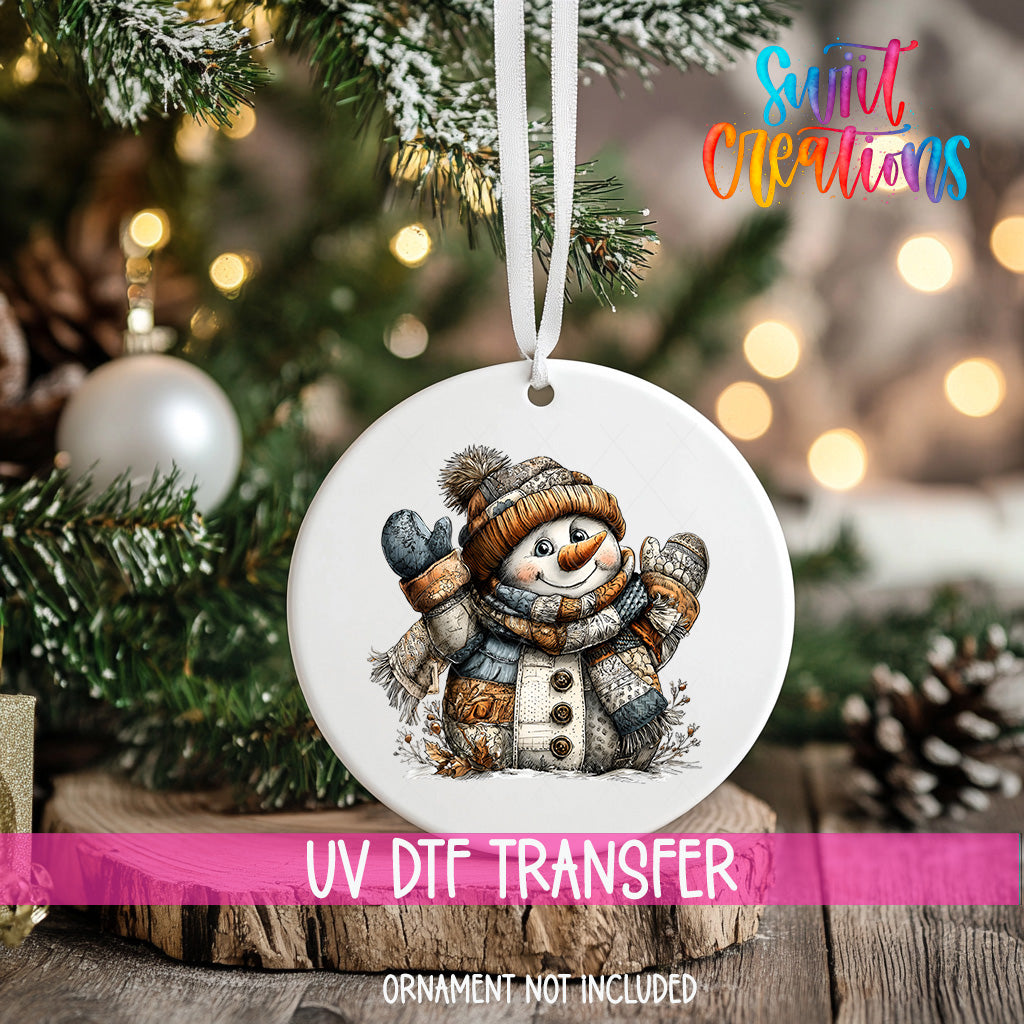 A white ornament with a snowman design hangs on a Christmas tree, surrounded by pine branches and twinkling lights.