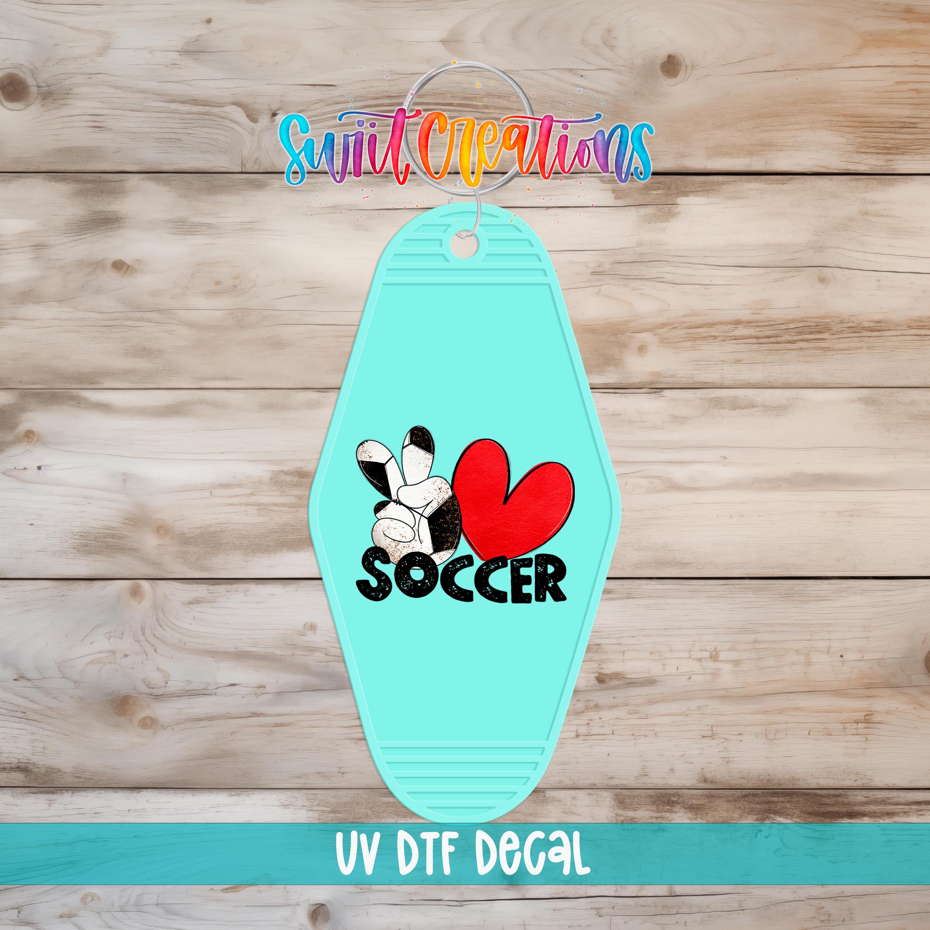 A turquoise keychain with a soccer-themed design, including a heart and the word "SOCCER".