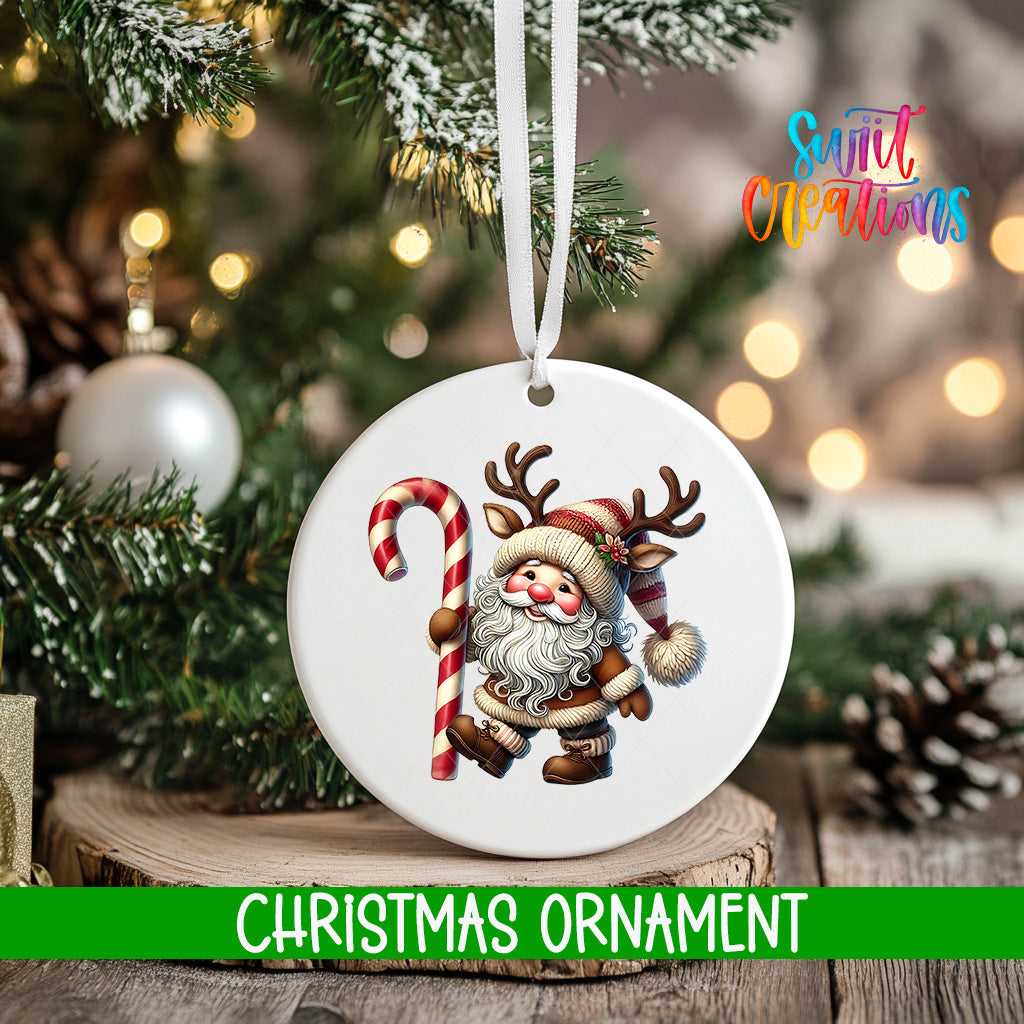 A white Christmas ornament featuring a Santa Claus figure holding a candy cane, with a blurred background of a decorated Christmas tree and other ornaments.