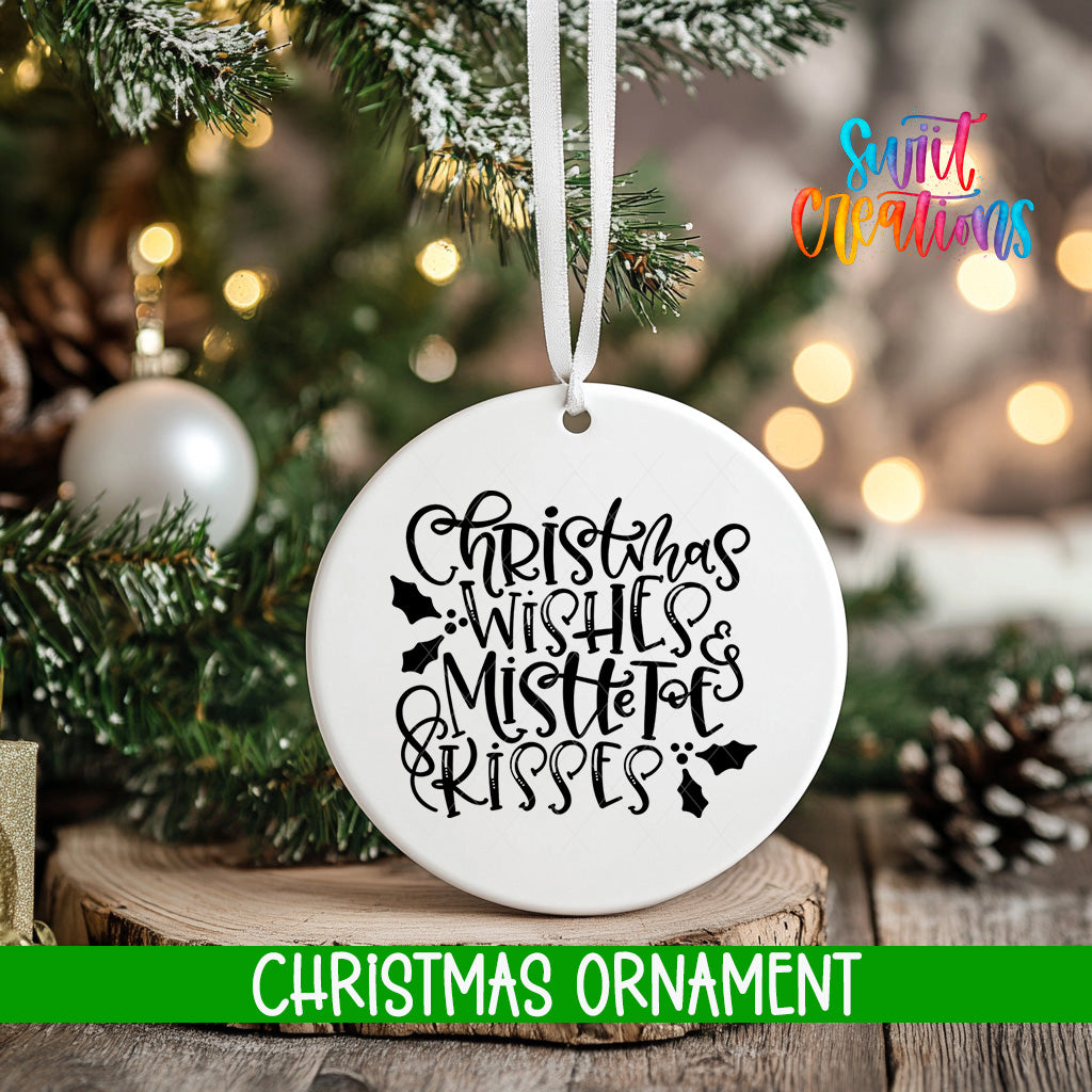 A white Christmas ornament with the text "Christmas Wishes & Mistle toes & kisses" hanging from a tree branch.