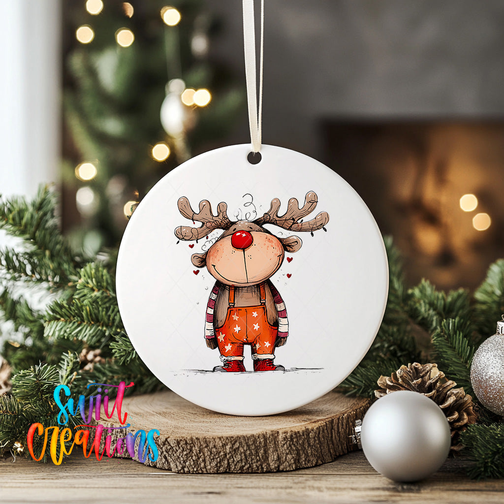 A white ceramic ornament featuring a cartoon reindeer with antlers and a red nose, surrounded by Christmas decorations and greenery.