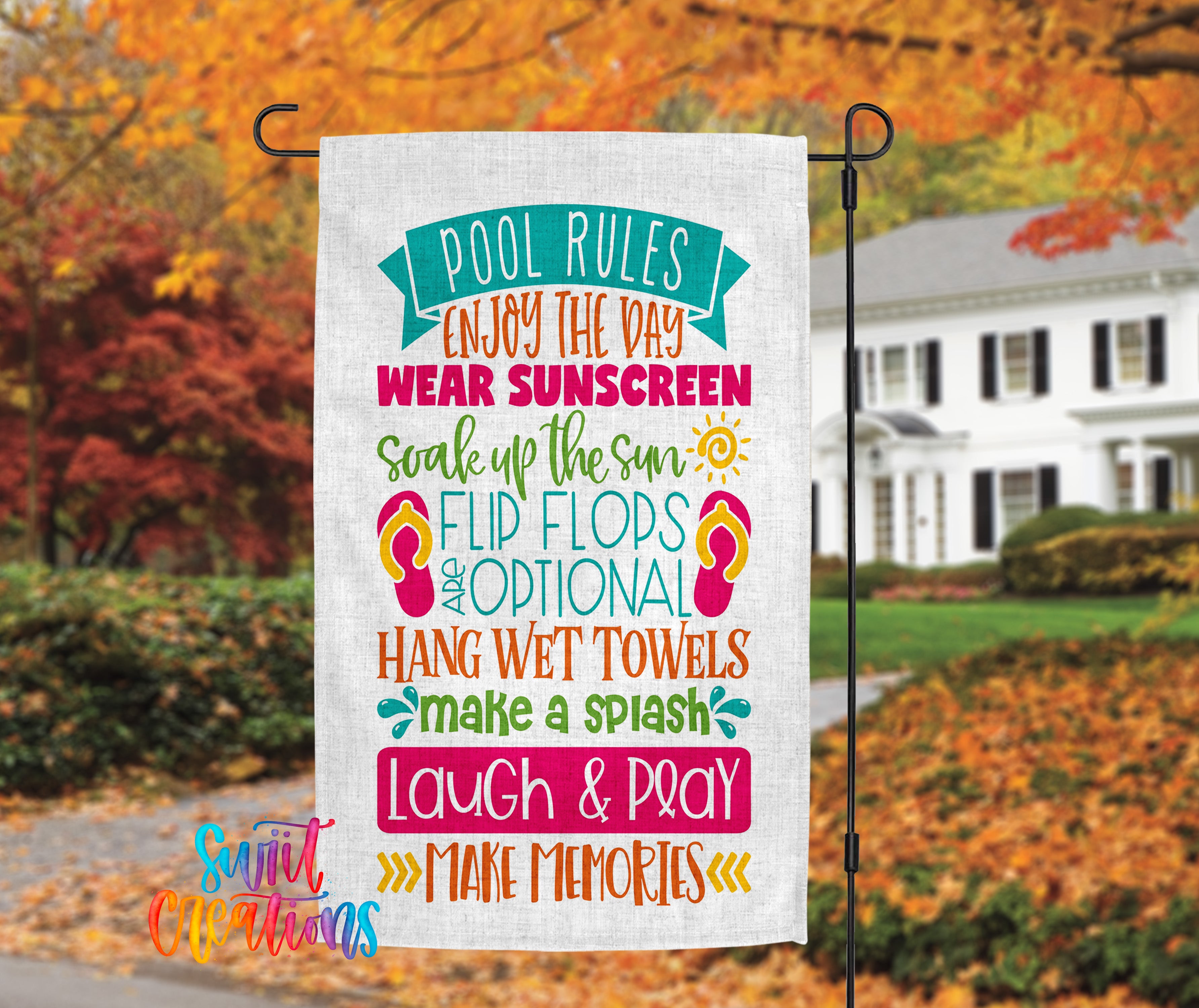 A colorful sign with text that reads "POOL RULES ENJOY THE DAY WEAR SUNSCREEN SWEAT UP THE SUN FLIP FLOPS AND OPTIONAL HANG WET TOWELS MAKE A SPASH LAUGH & PRAY MAKE MEMORIES" is displayed in front of a house with autumn foliage in the background.