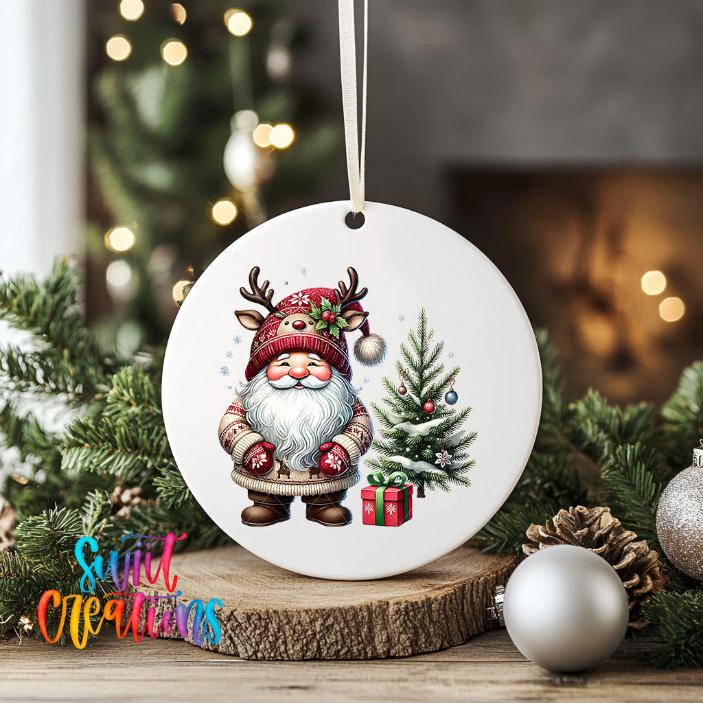 A white ceramic ornament featuring a Santa Claus figure with antlers and a Christmas tree, surrounded by pine cones and ornaments, placed on a wooden surface.