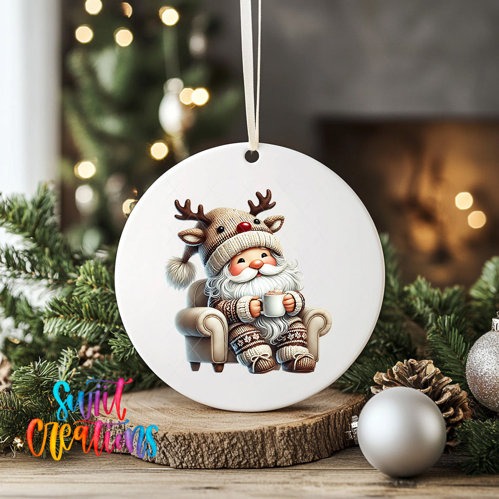 A white ceramic ornament featuring a cartoon reindeer sitting in a chair, holding a cup, is displayed on a wooden surface with Christmas decorations in the background.