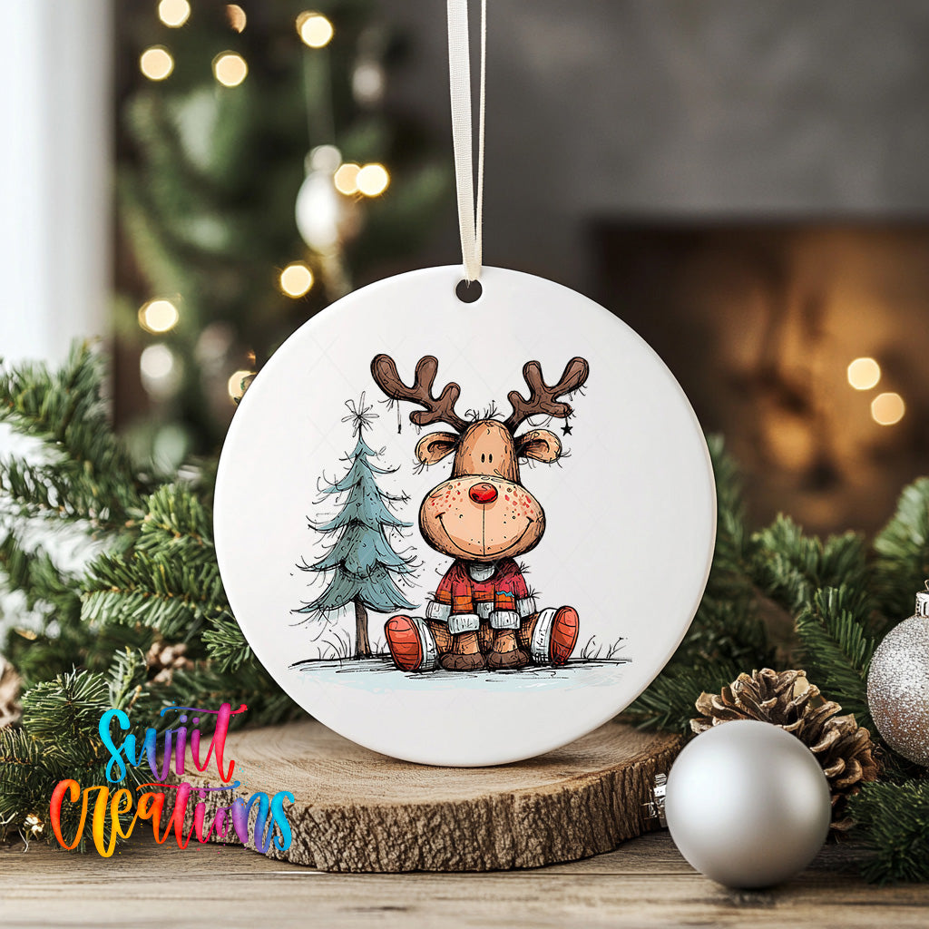 A white ceramic ornament featuring a cartoon reindeer sitting on a snowy landscape, surrounded by Christmas decorations and greenery.