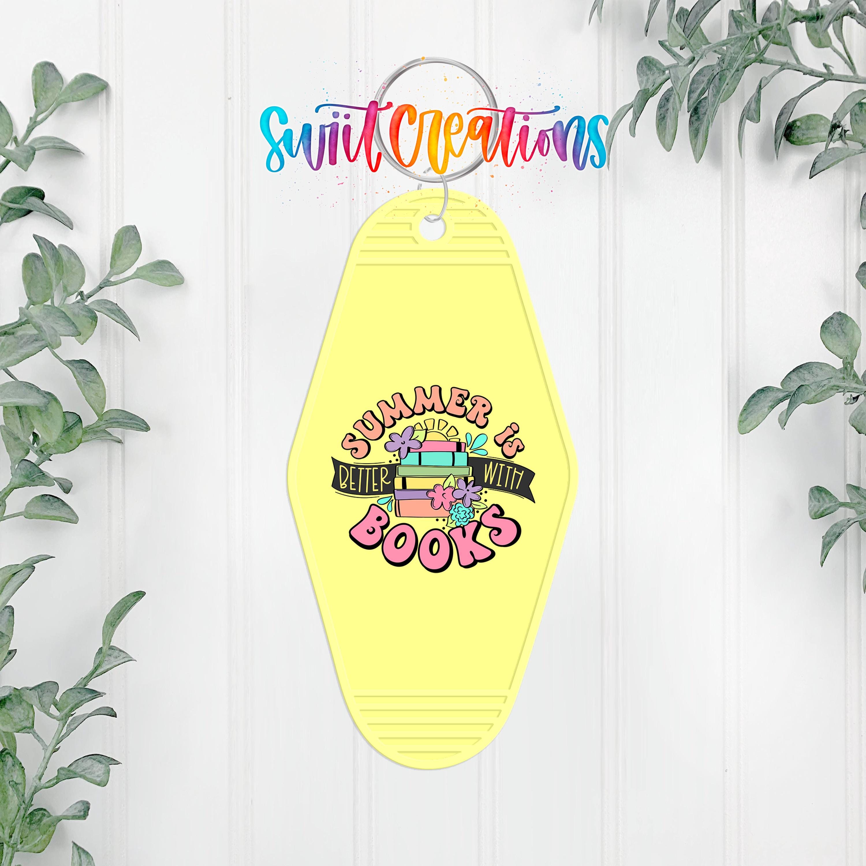 A yellow keychain with a colorful graphic design and text, hanging on a white wall with greenery in the background.