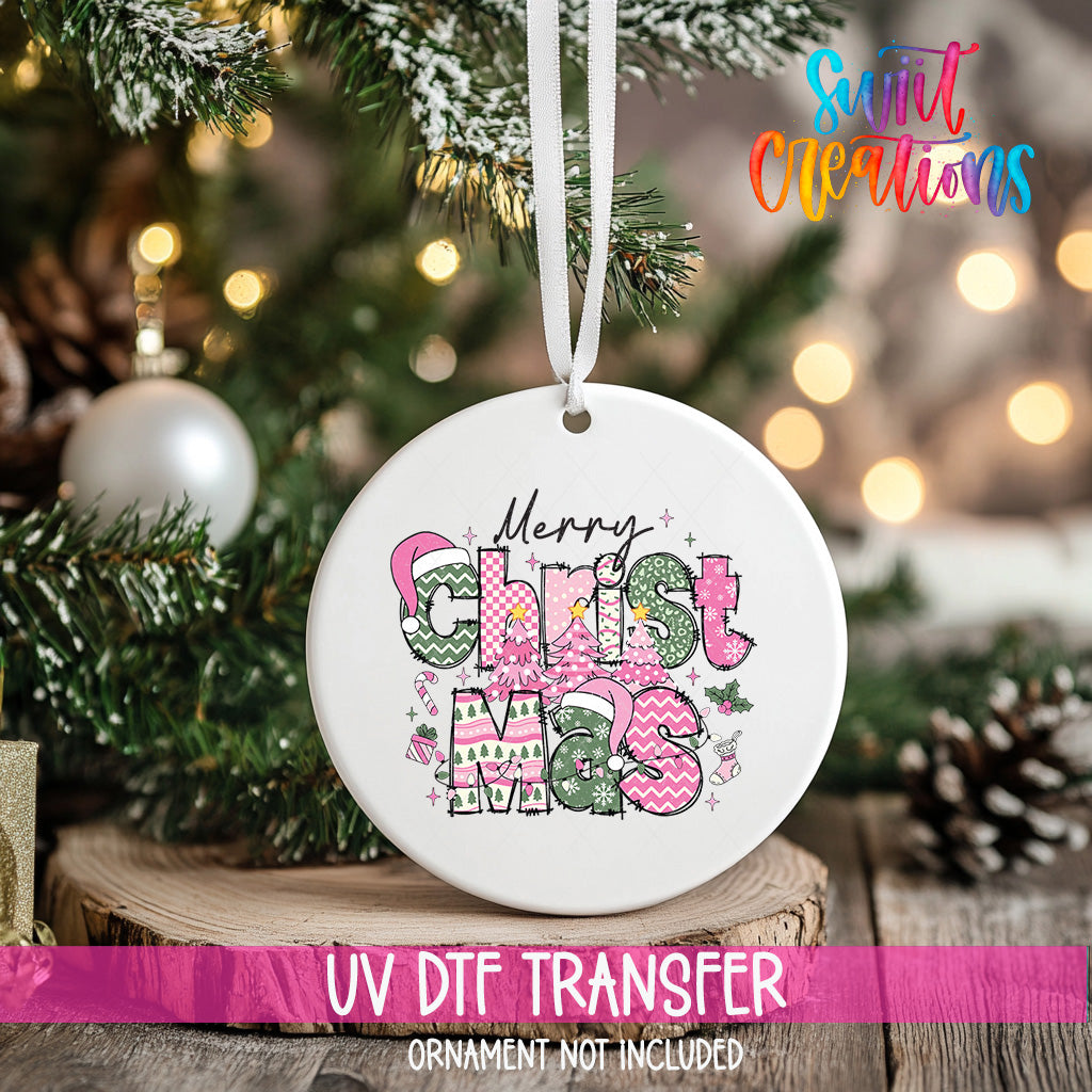 A white Christmas ornament with the text "Merry Christmas" in pink and green colors, hanging on a Christmas tree.