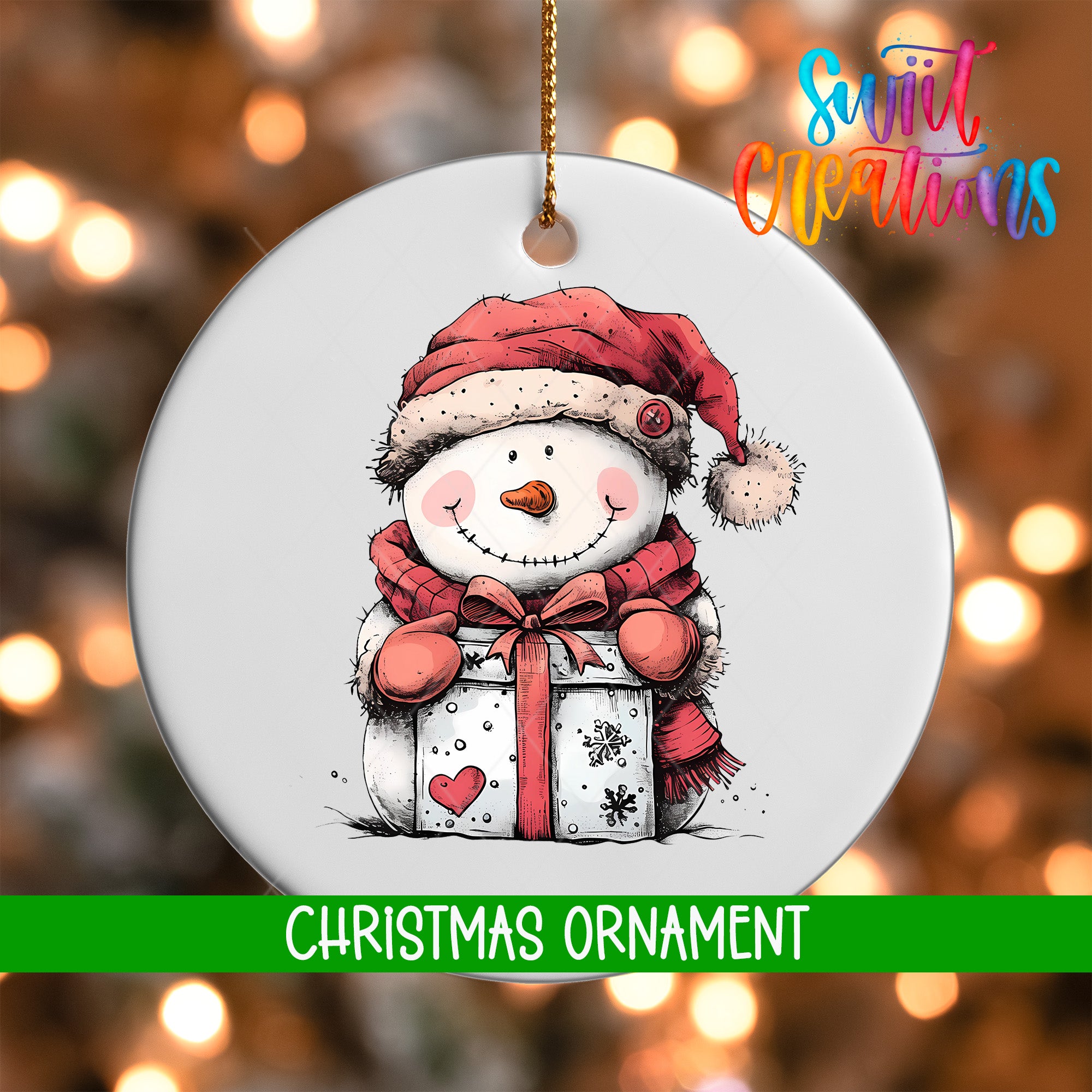 A white Christmas ornament featuring a snowman holding a gift box, with a red scarf and hat, against a blurred background of Christmas lights.