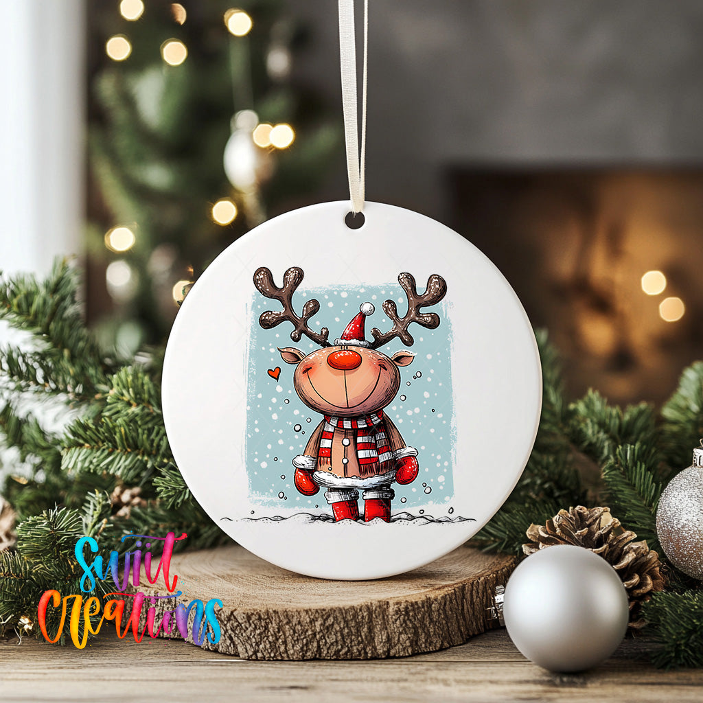A white ceramic ornament featuring a cartoon reindeer with antlers, wearing a red scarf and standing in the snow, is displayed on a wooden surface.