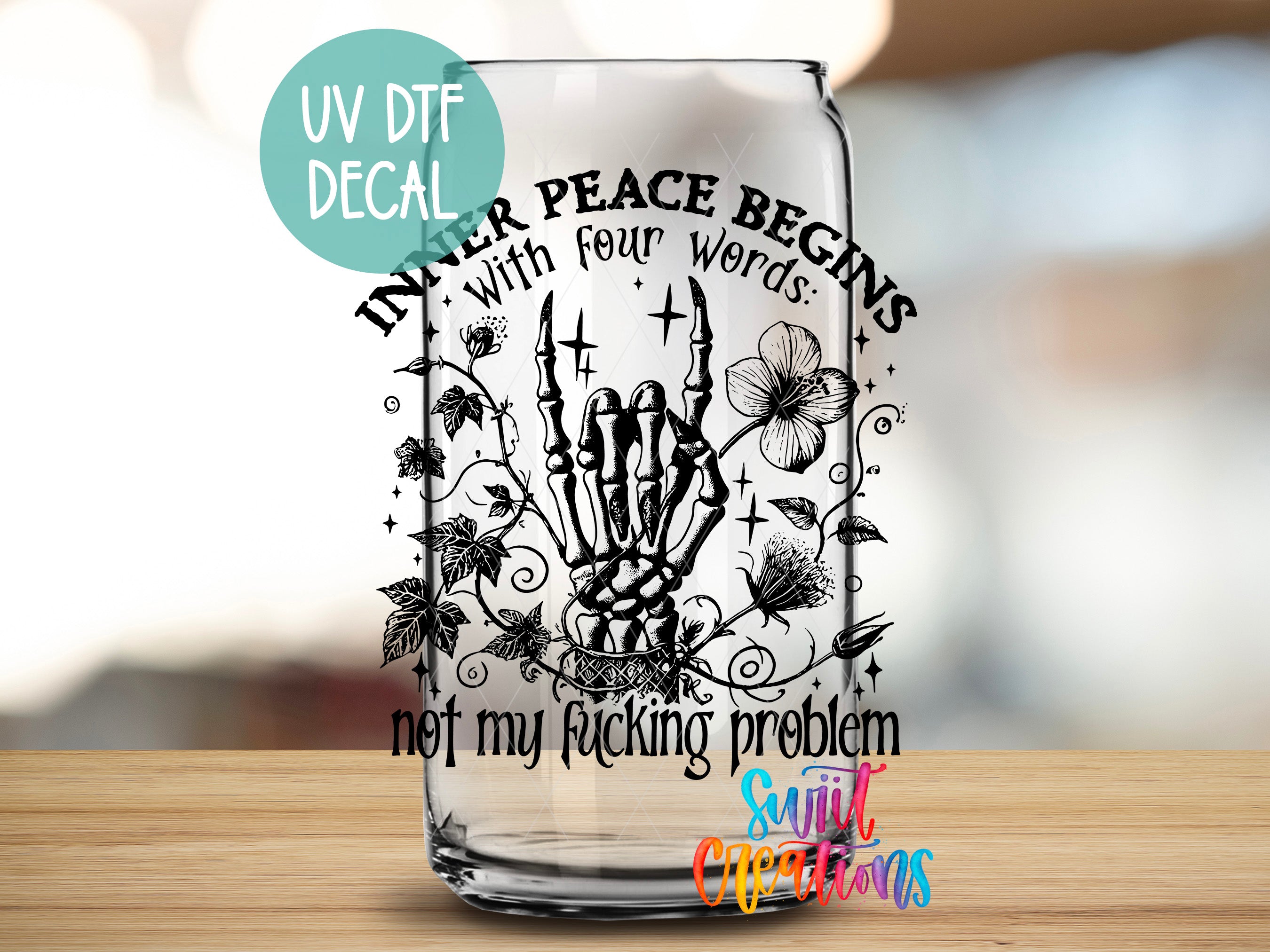 A glass with a black and white graphic design featuring a skeleton hand holding a flower, surrounded by leaves and other floral elements. The text on the glass reads "Inner Peace Begins with four words: not my Fucking problem" and "Sunlit Creations".