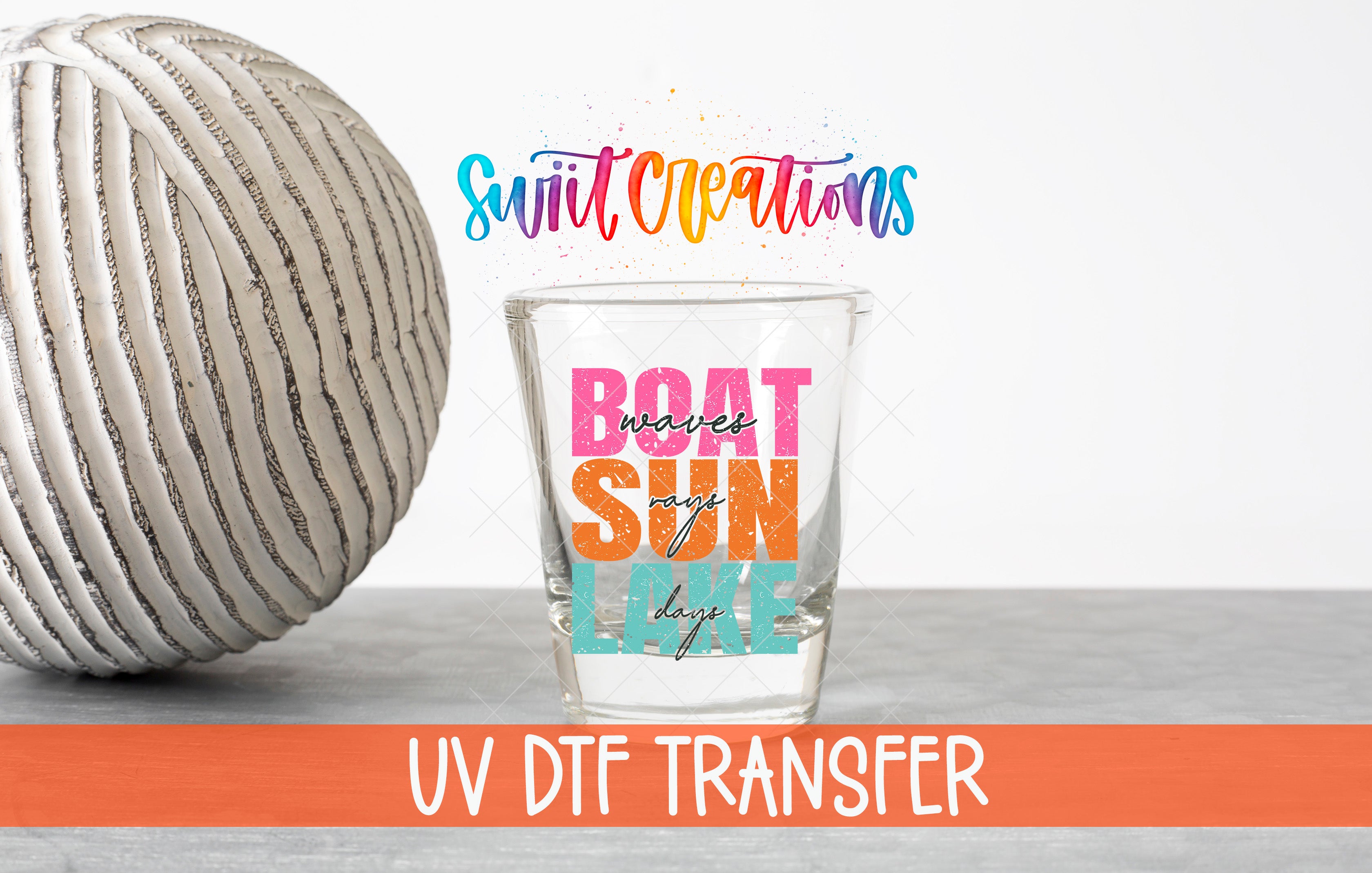 a glass with a colorful design and text, placed next to a white ball on a gray surface.