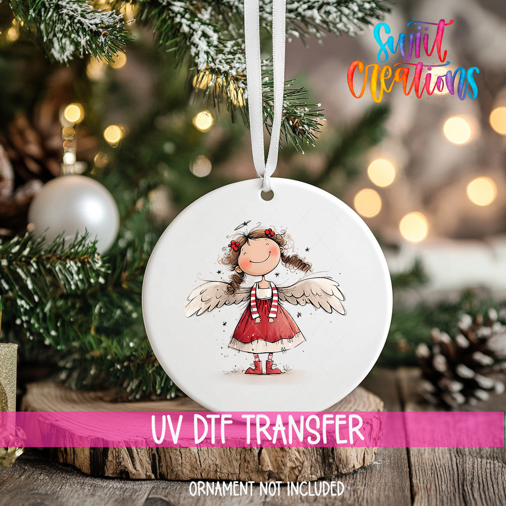 A white ornament with a smiling girl wearing a red dress and wings, hanging on a Christmas tree.