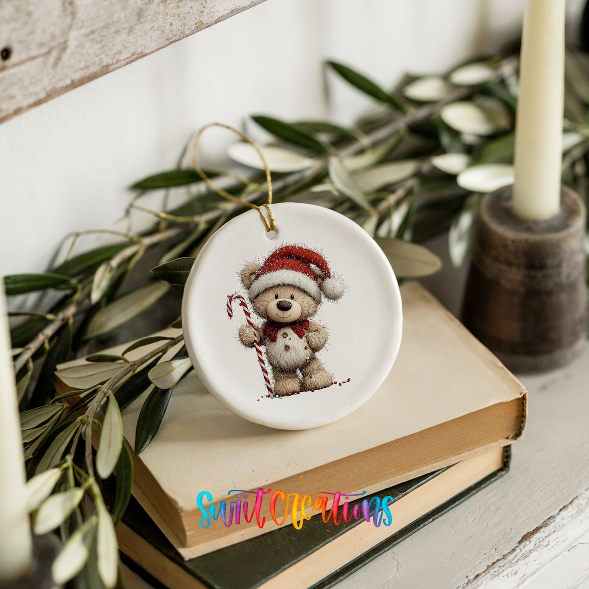 teddy bear wearing a Santa hat and holding a candy cane ceramic Christmas ornament styled on stacked books with greenery