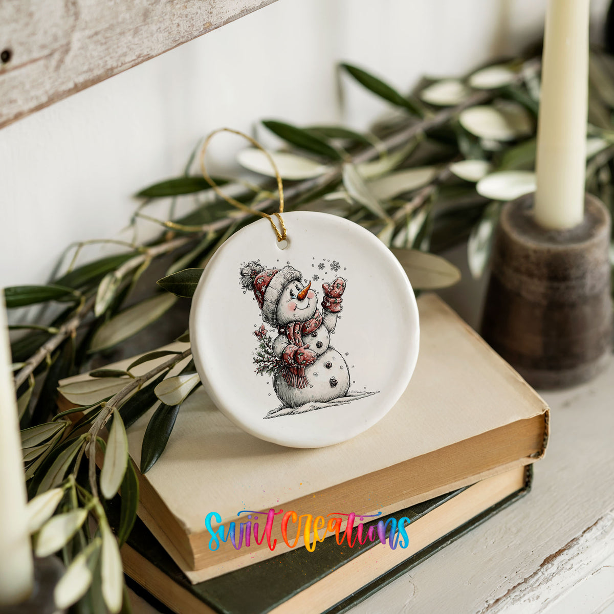 snowman holding a snowy Christmas tree ceramic Christmas ornament styled on stacked books with greenery