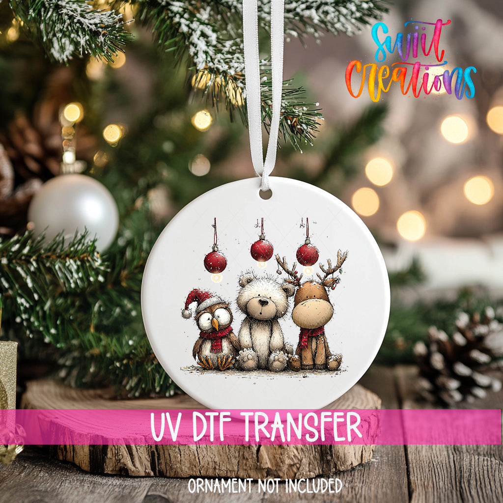 A white ornament with a Christmas tree and ornaments, including a bear, reindeer, and owl, hanging from a ribbon.