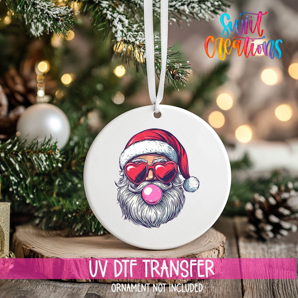 A white ornament with a Santa Claus face wearing sunglasses and a red hat, along with a pink bubblegum bubble, is hanging from a Christmas tree.