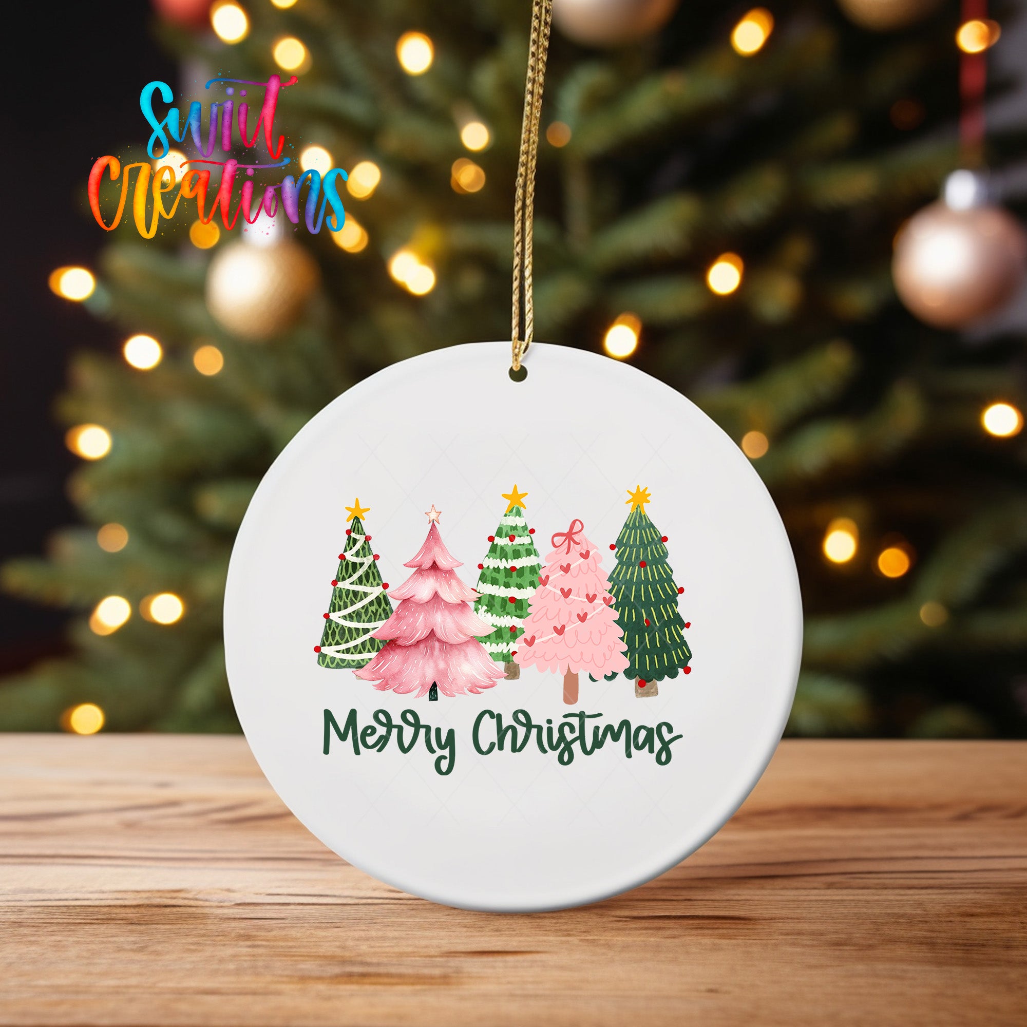 A white ceramic ornament with a festive Christmas tree design hangs on a wooden surface, with a blurred background of twinkling lights.