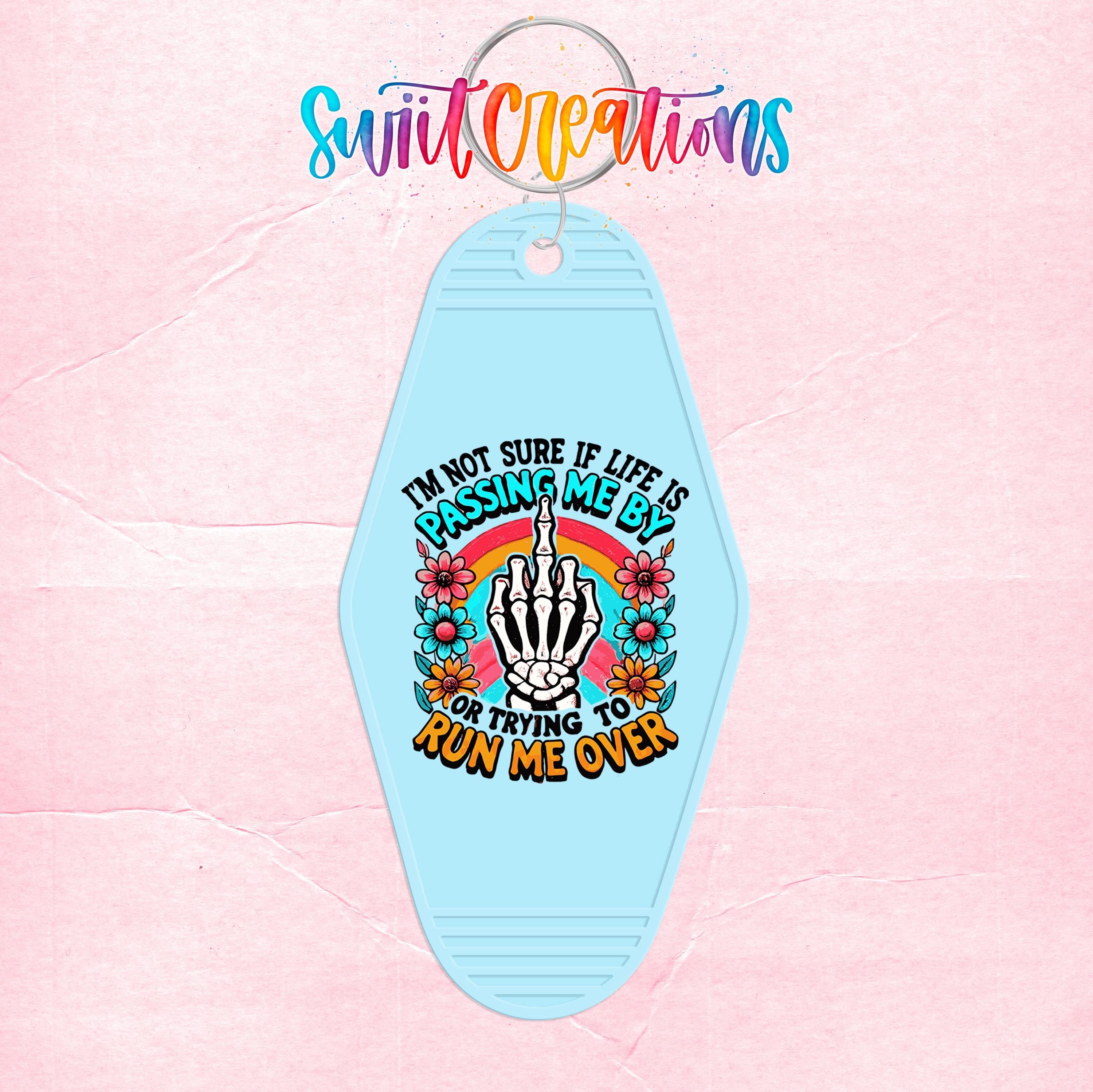 A keychain with a colorful design featuring a skeleton hand and text that reads "I'm not sure if life is passing me by or trying to run me over".