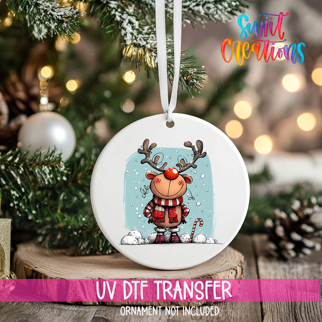 A white ceramic ornament with a cartoon reindeer and snowflakes hanging on a Christmas tree.