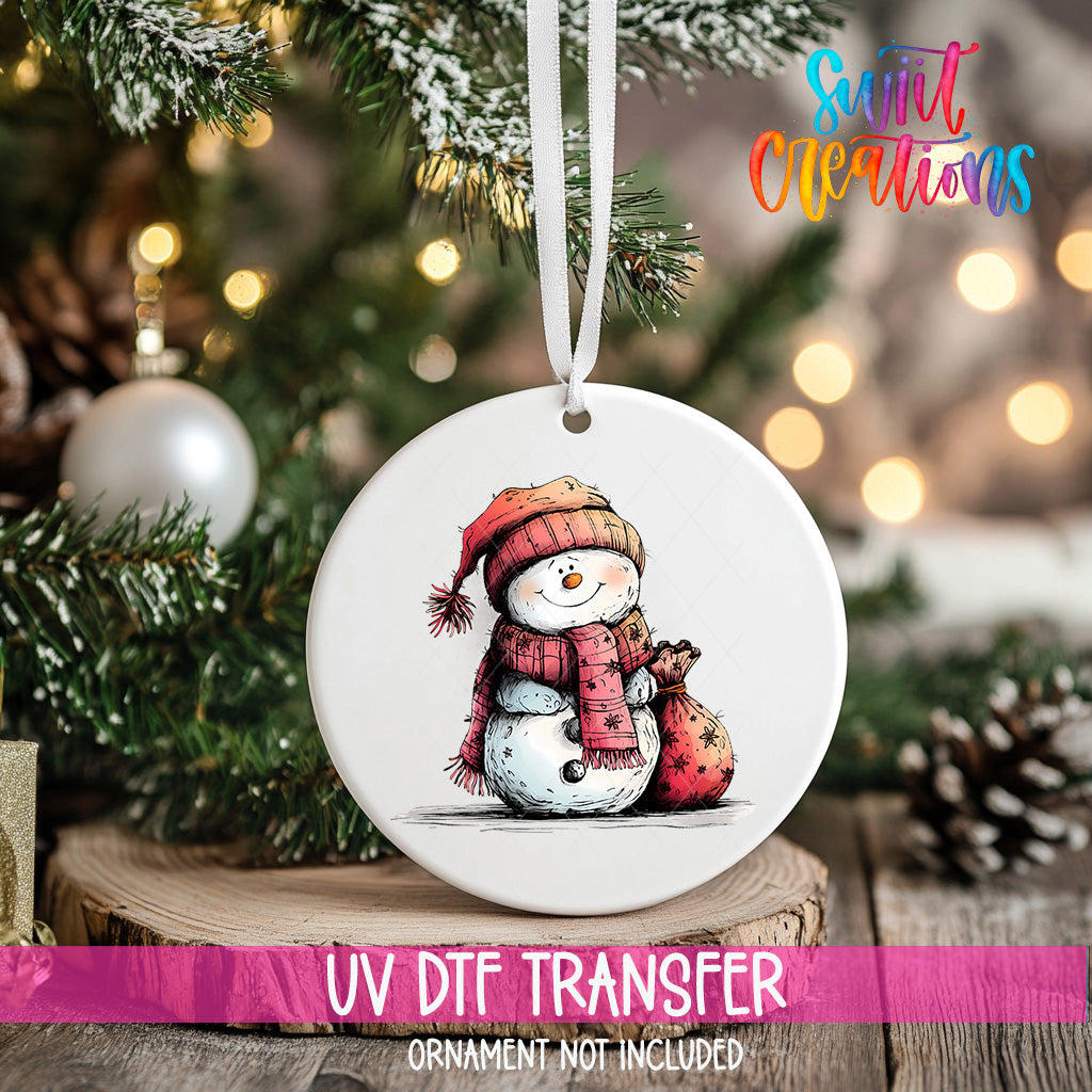 A white ceramic ornament featuring a snowman is hanging on a Christmas tree, with a blurred background of pine branches and twinkling lights.
