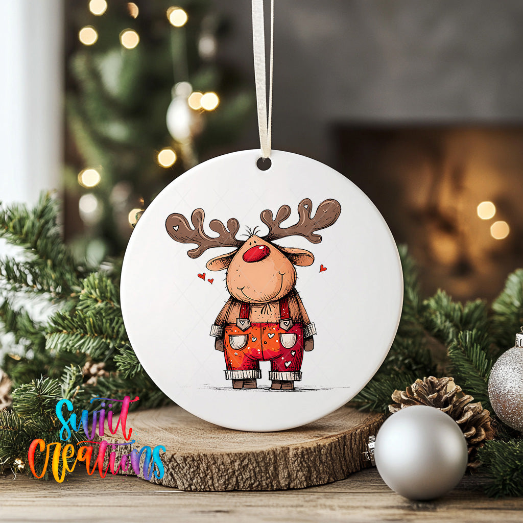 A white ceramic ornament featuring a cartoon reindeer with antlers and a red nose, surrounded by Christmas decorations such as pine cones and ornaments.