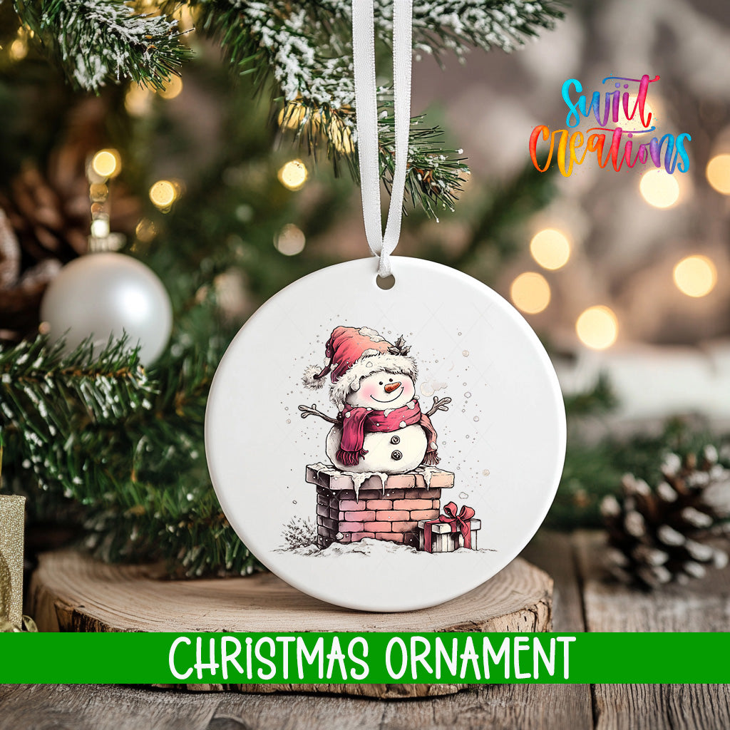 A white Christmas ornament featuring a snowman is hanging from a tree branch, with a blurred background of a decorated Christmas tree and other ornaments.