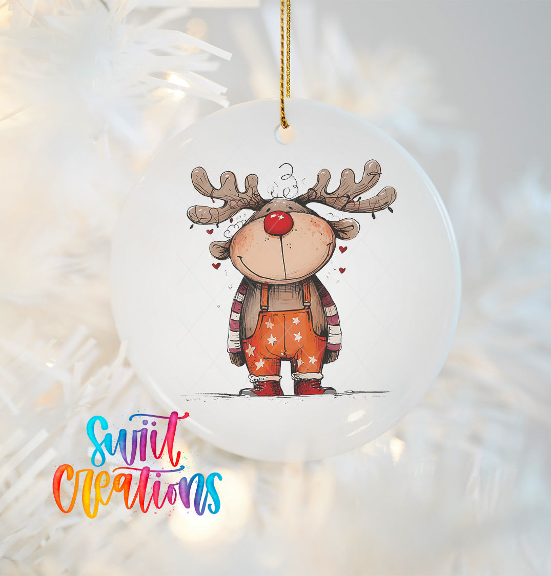 A white ornament featuring a cartoon reindeer with antlers and a red nose, hanging on a Christmas tree.