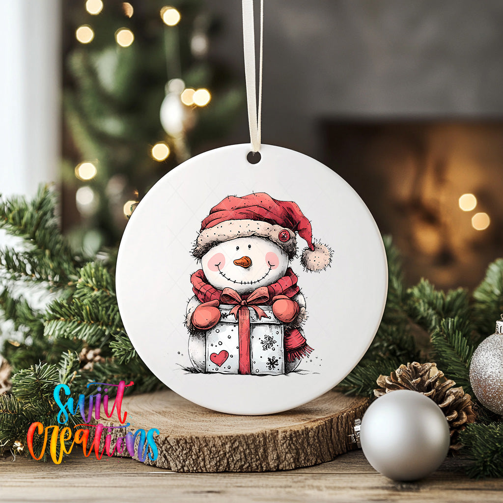 A white ceramic ornament featuring a snowman wearing a red hat and scarf, holding a gift box, is displayed on a wooden surface with Christmas decorations in the background.