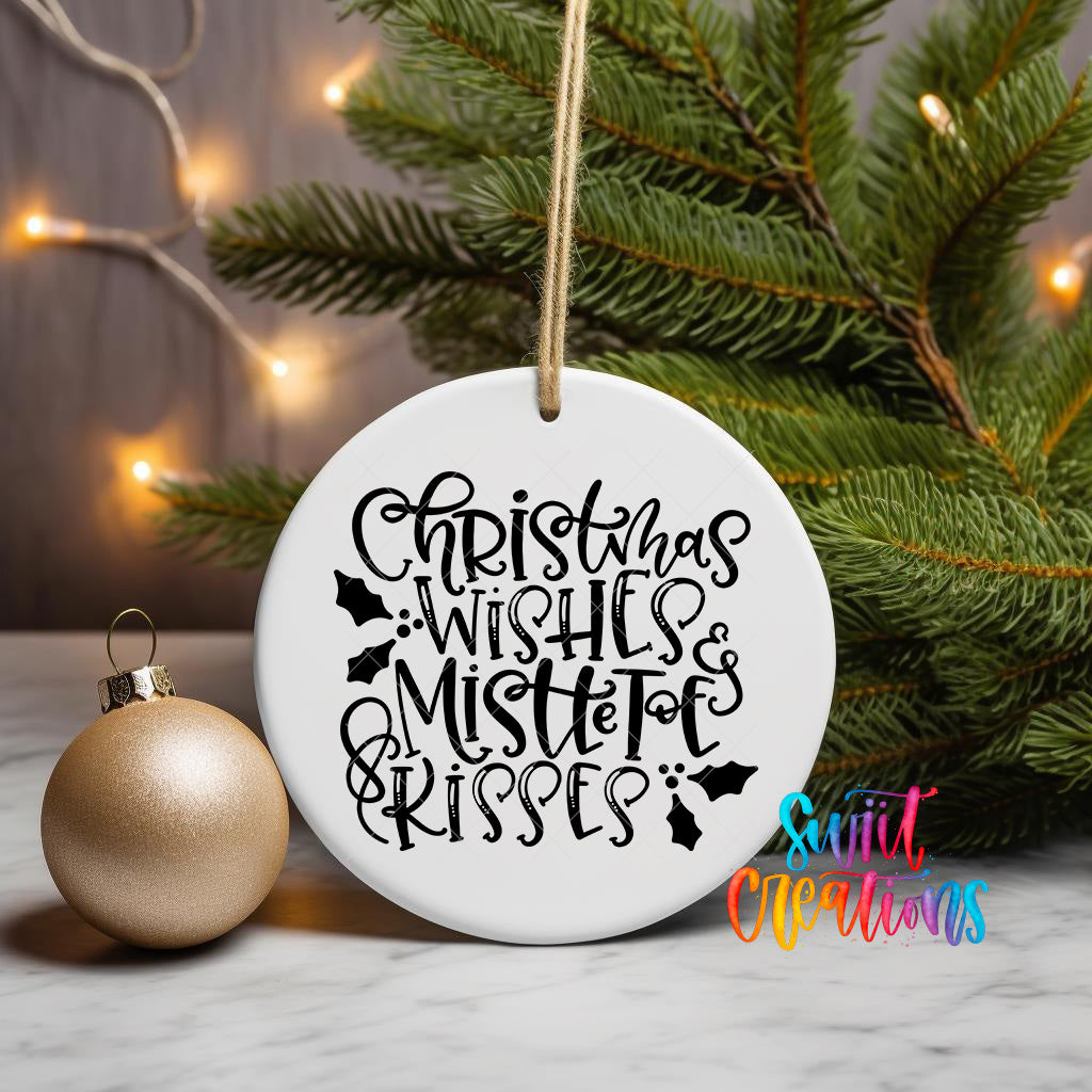 A white ceramic ornament with the text "Christmas Wishes, Mistletoe & Kisses" written on it, hanging from a string next to a gold ornament and a Christmas tree.