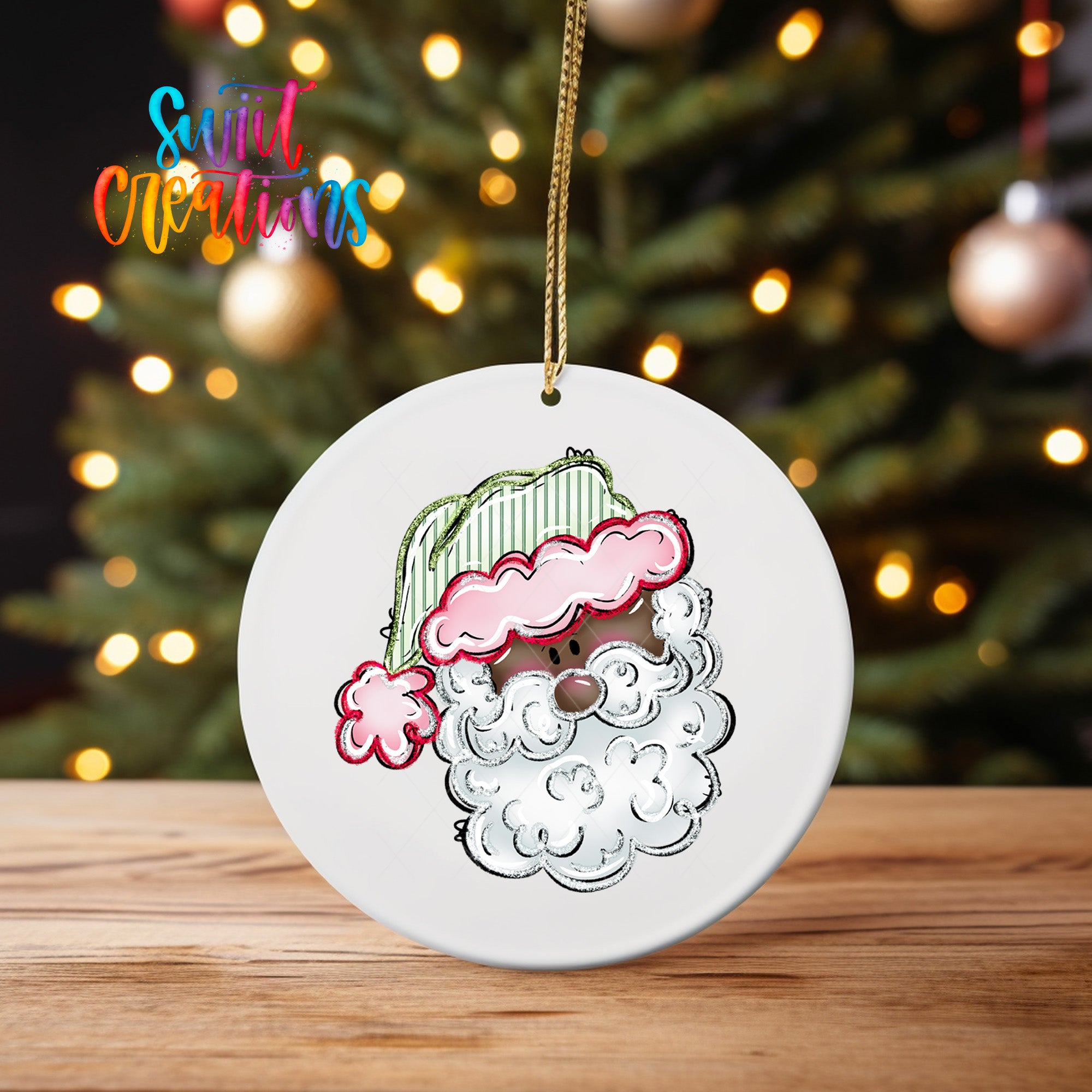 A white ceramic ornament with a Santa Claus face design hangs on a wooden surface, with a blurred background of a Christmas tree and twinkling lights.