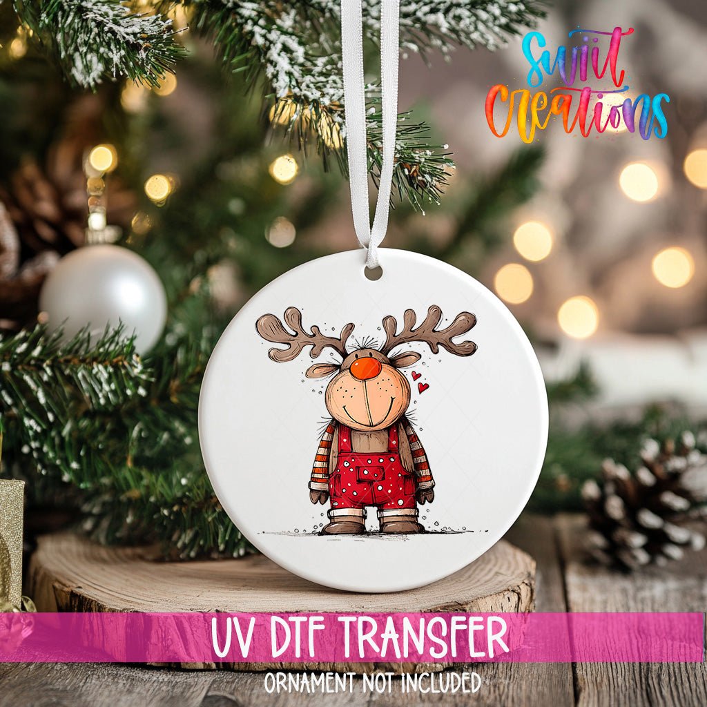 A white ceramic ornament with a cartoon reindeer design hangs on a Christmas tree.