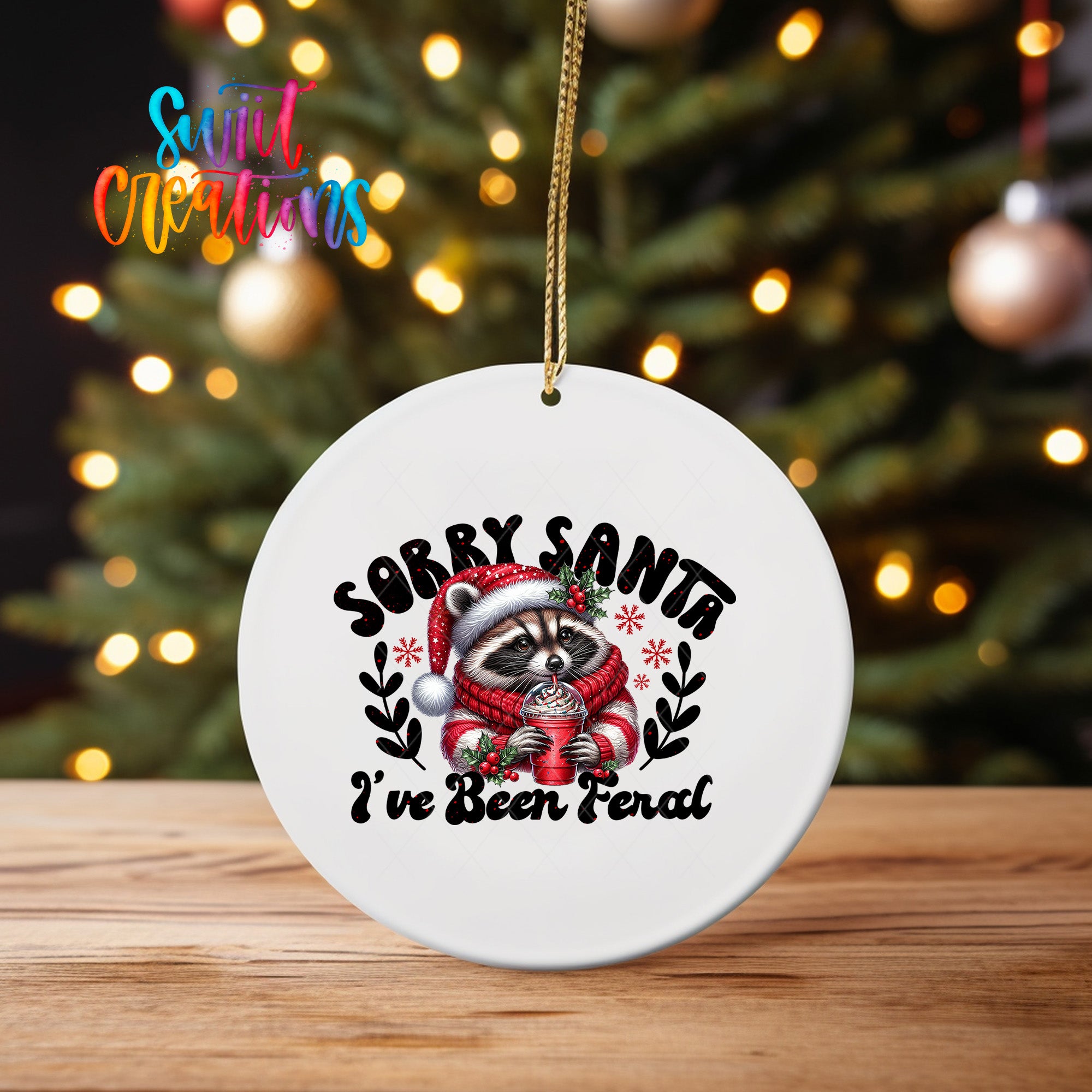 A white ornament with a raccoon wearing a Santa hat and scarf, holding a cup of hot chocolate, and the text "Sorry Santa I've Been Feral" printed on it.