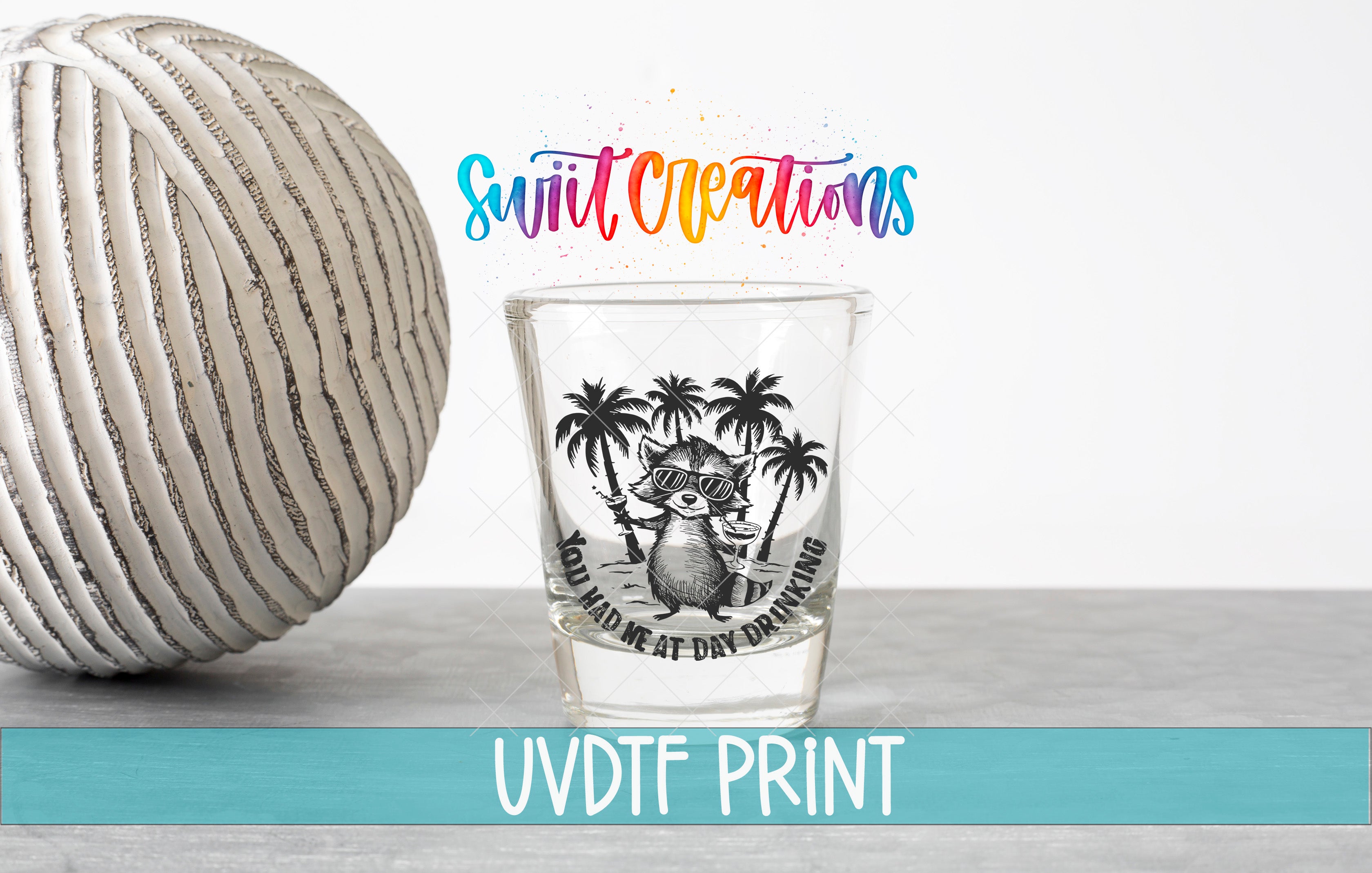 a shot glass with a graphic design and text, placed on a table next to a striped ball.