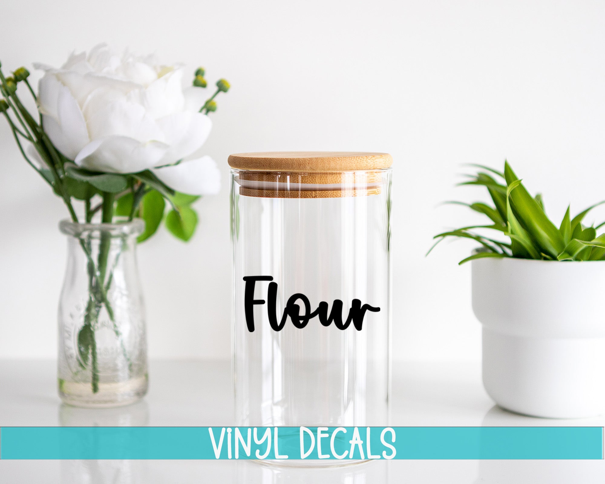 a clear glass jar with a wooden lid, a glass vase with white flowers, and a white pot with a green plant, all placed on a white surface.