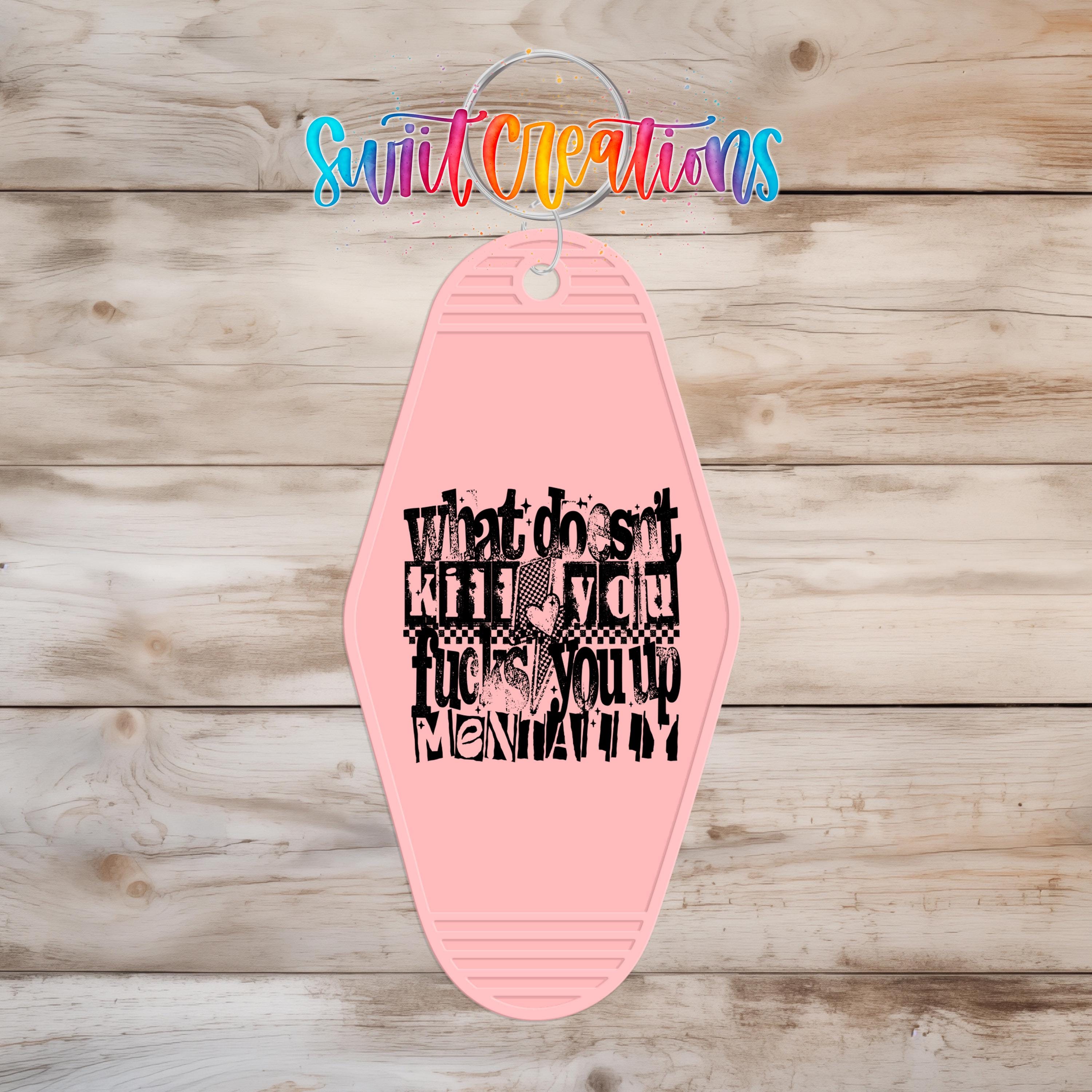 A pink keychain with a black text design on it, hanging on a wooden surface.