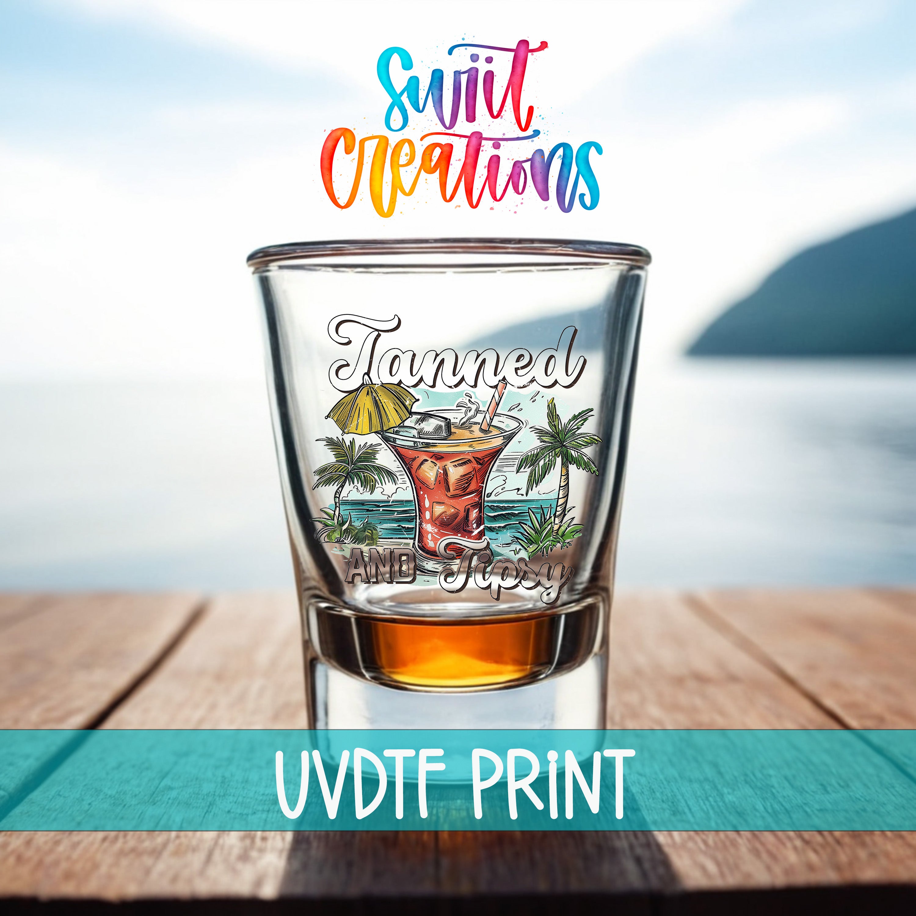 A shot glass with a tropical drink design and the text "Tanned and sticky" printed on it, placed on a wooden surface with a body of water in the background.