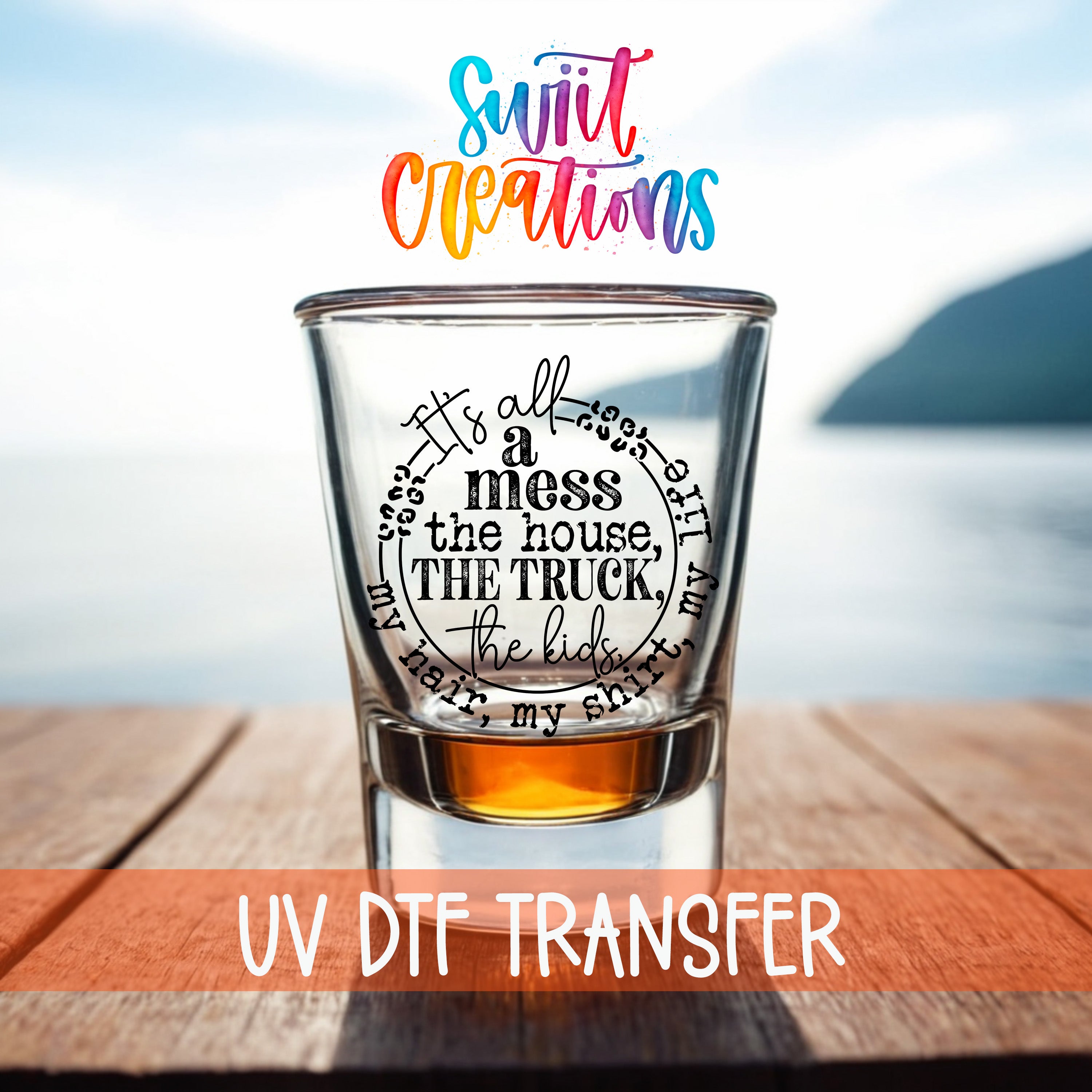 a shot glass with a message printed on it, placed on a wooden surface with a body of water in the background.
