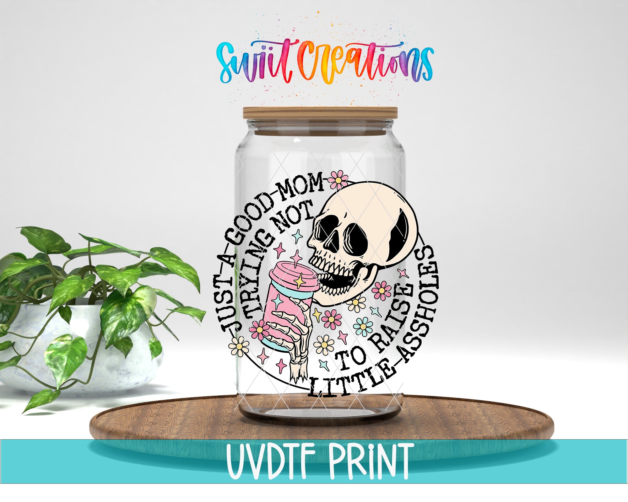 A glass jar with a skull design and text, placed on a wooden surface next to a potted plant.