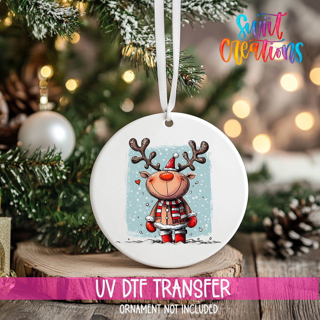 A white ceramic ornament with a cartoon reindeer and snowflakes hanging on a Christmas tree.