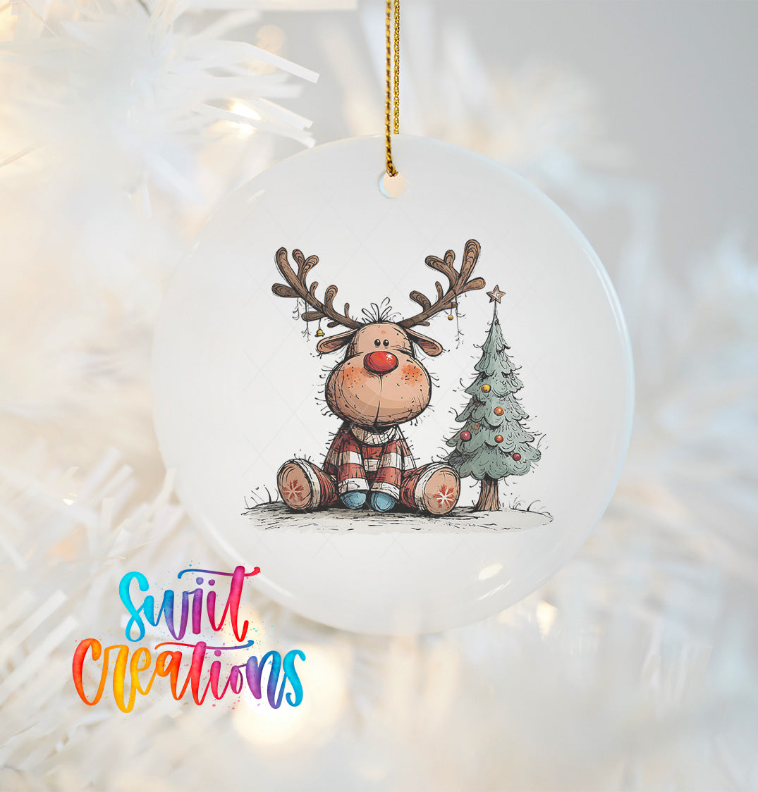 A white ornament with a cartoon reindeer and a Christmas tree on it, hanging on a string.