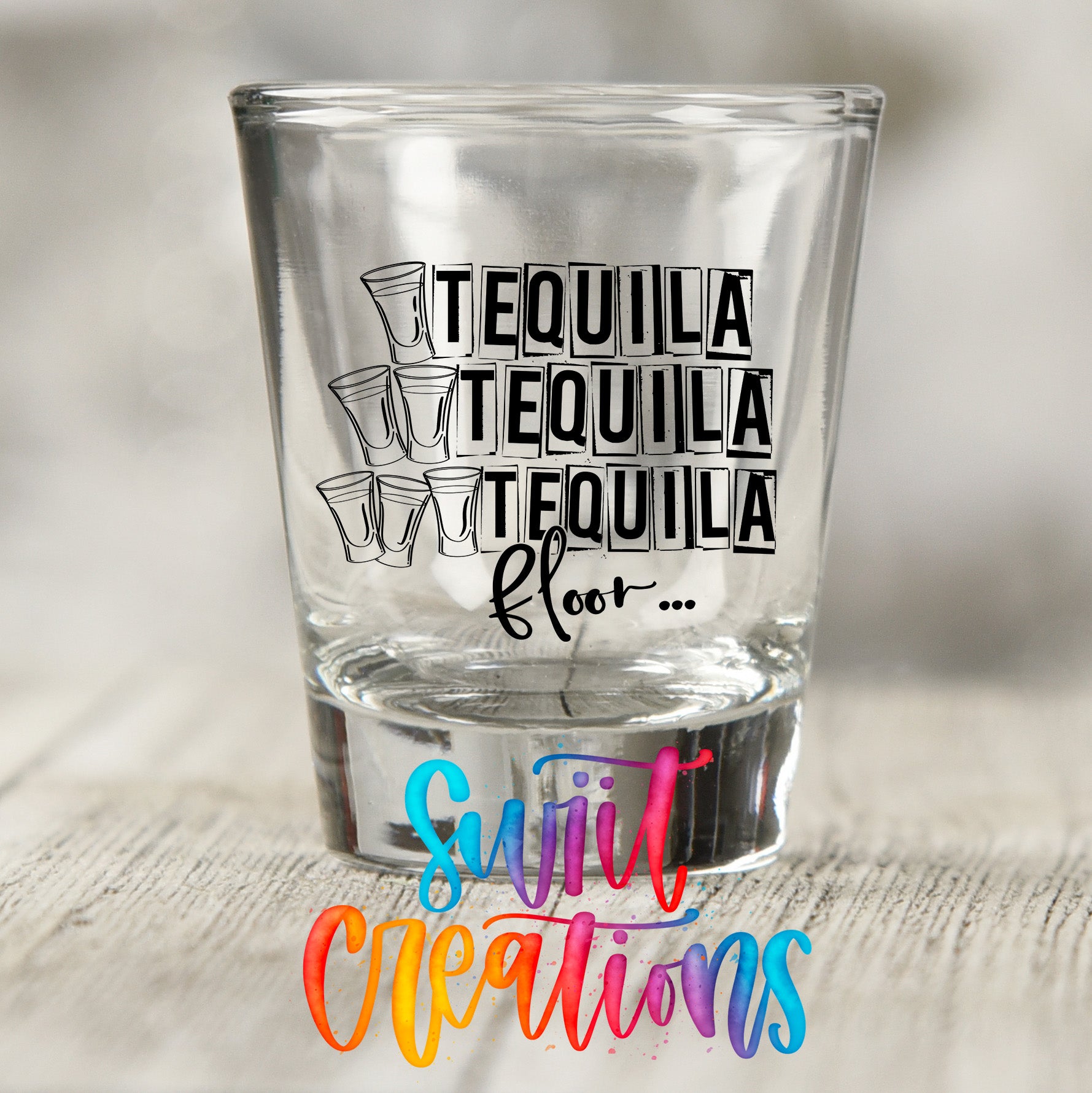 A clear shot glass with the text "TEQUILA TEQUILA TEQUILA" printed on it, along with a colorful watermark that says "Sult Creations" in the bottom right corner.