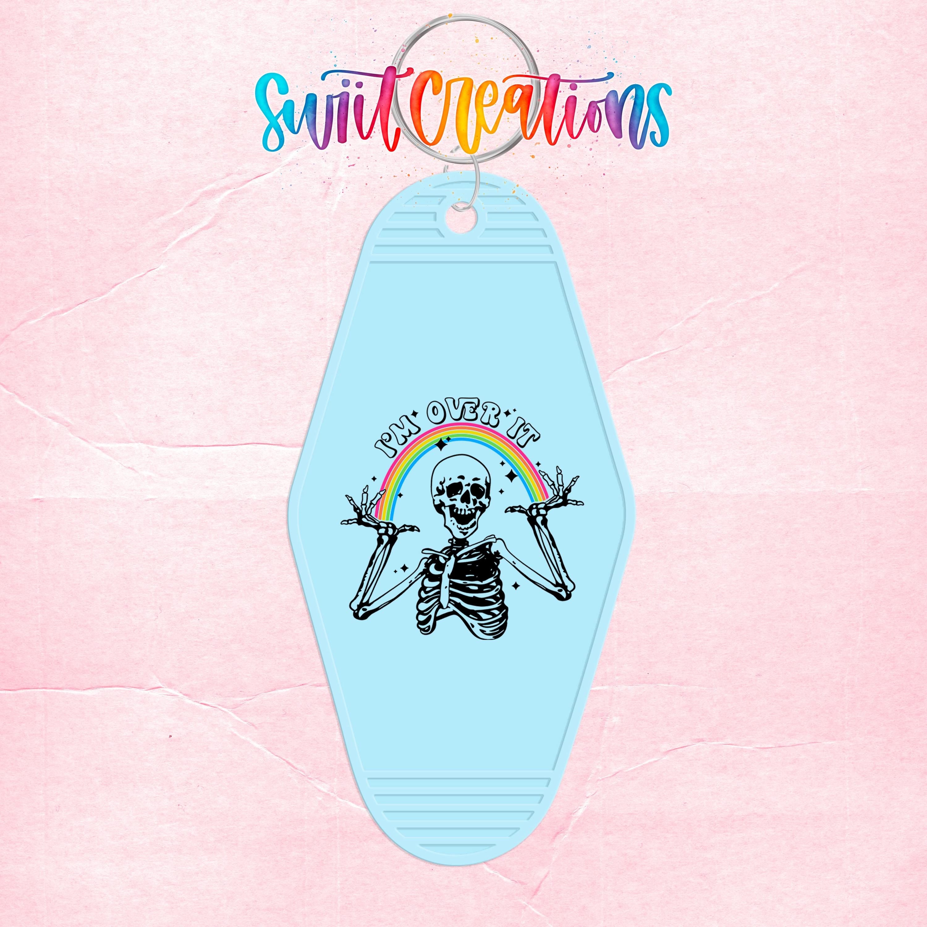A keychain with a skeleton graphic and a rainbow graphic, along with the text "I'm over it" and a rainbow symbol.