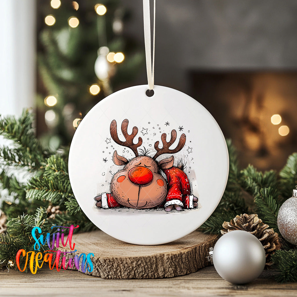 A white ornament with a cartoon reindeer and snowflakes is displayed on a wooden surface, surrounded by Christmas decorations and greenery.
