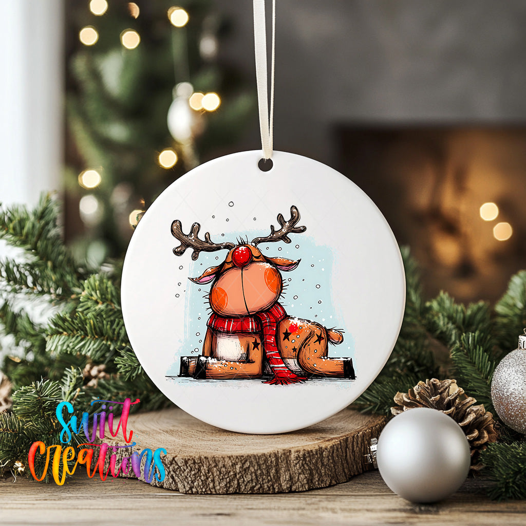 A white ceramic ornament featuring a cartoon reindeer with antlers, wearing a red scarf, is displayed on a wooden surface with Christmas decorations in the background.