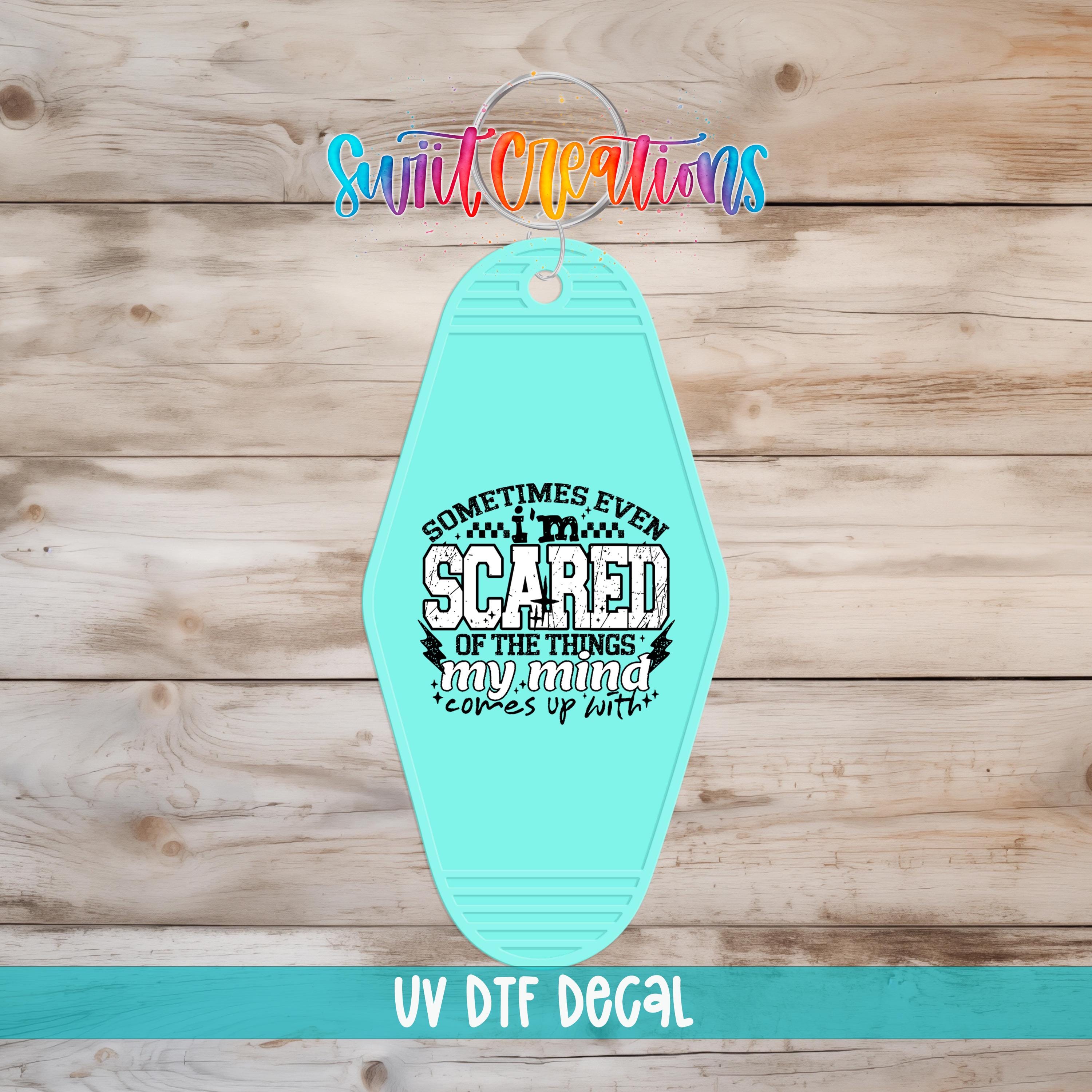 A turquoise keychain with a printed message on it, displayed on a wooden background.