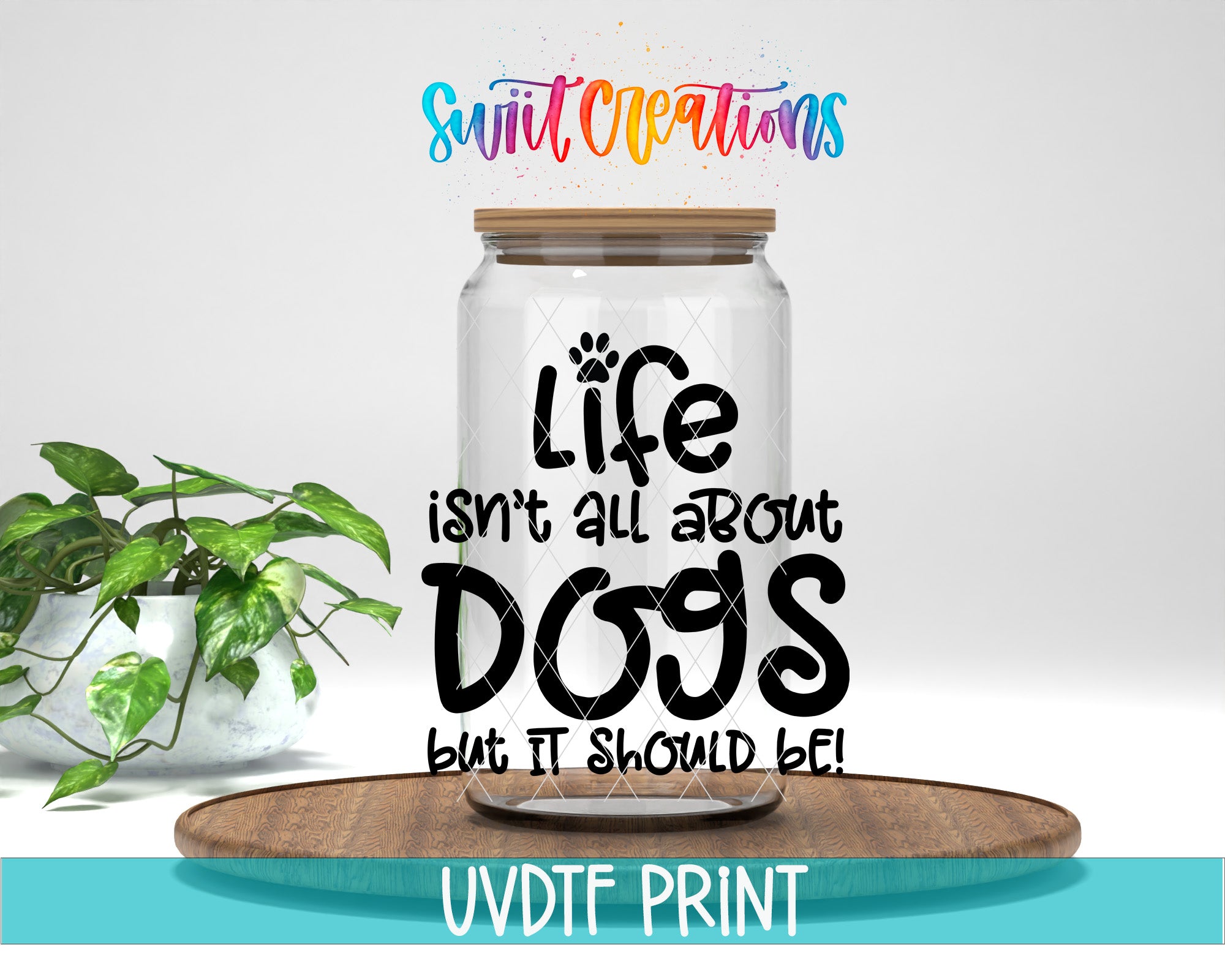 a clear glass jar with a wooden lid, placed on a wooden tray. The jar has a message written on it in a playful font, which reads "Life isn't all about dogs but it should be!" The background of the image is white, and there is a potted plant to the left of the jar.